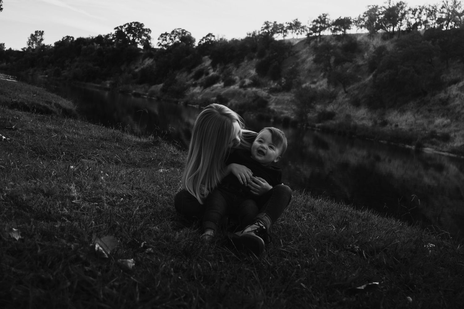Couple lying together on grassy hillside at sunset in romantic outdoor setting.