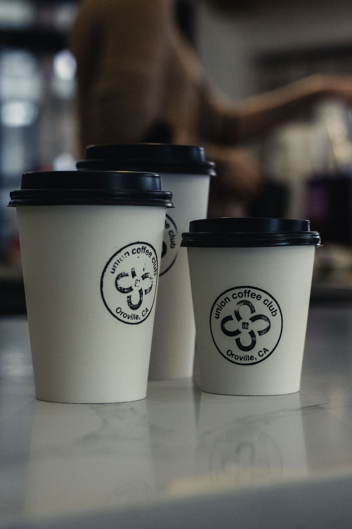 Row of white coffee cups with black lids featuring cafe logo designs.