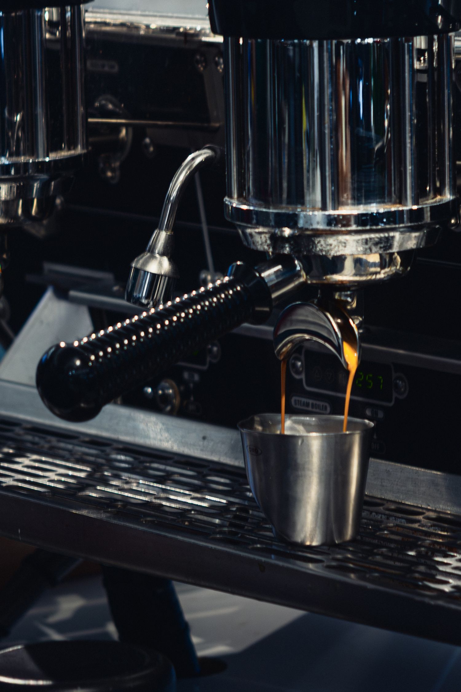 Espresso machine pouring dark coffee into a metal container.