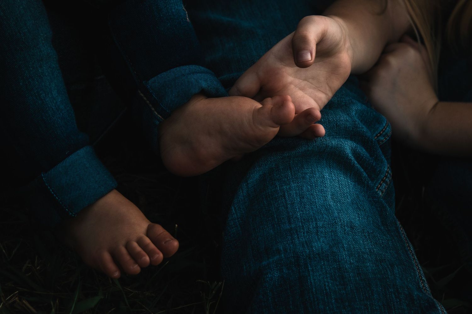 Intimate family portrait showing playful interaction on grass near water.