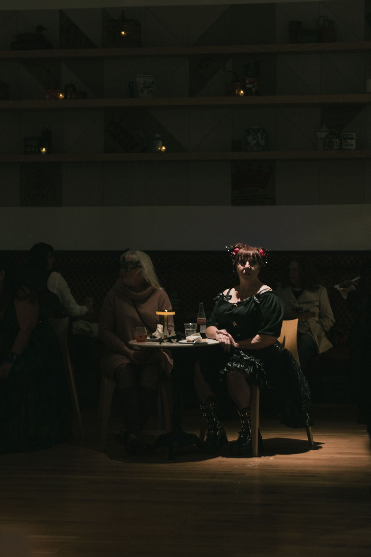 Two women sit at a candlelit table in a dimly lit restaurant, one wearing a floral crown.
