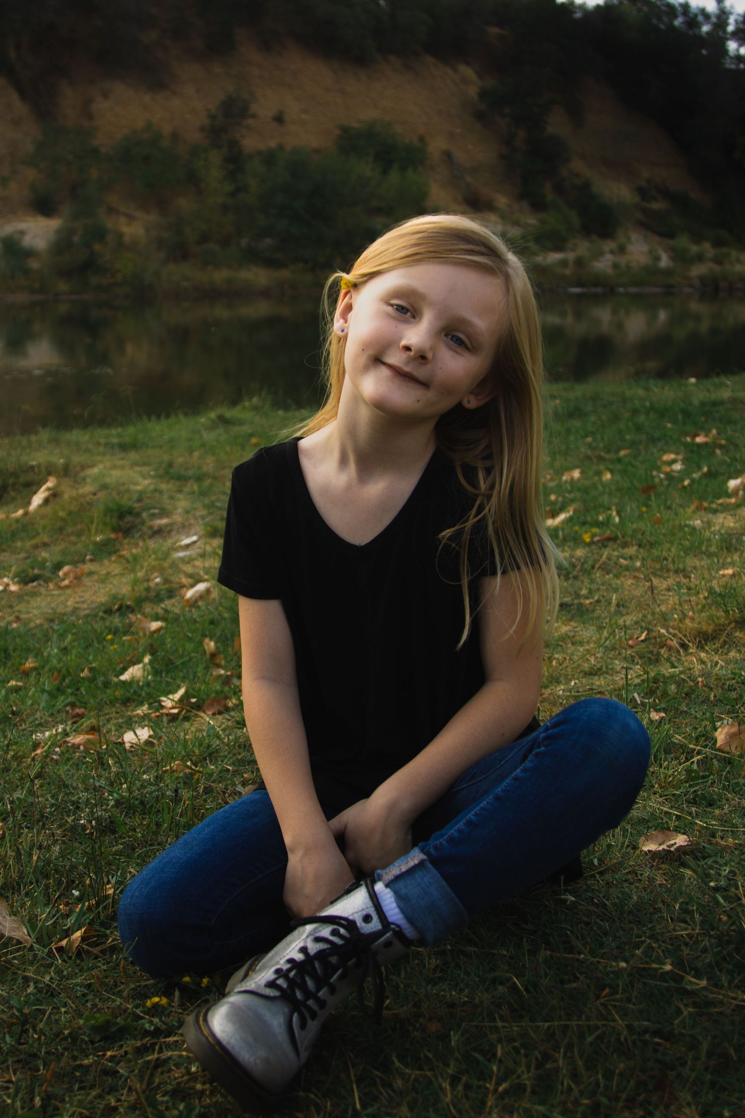 Child in black shirt and jeans sitting on grass with a playful expression.