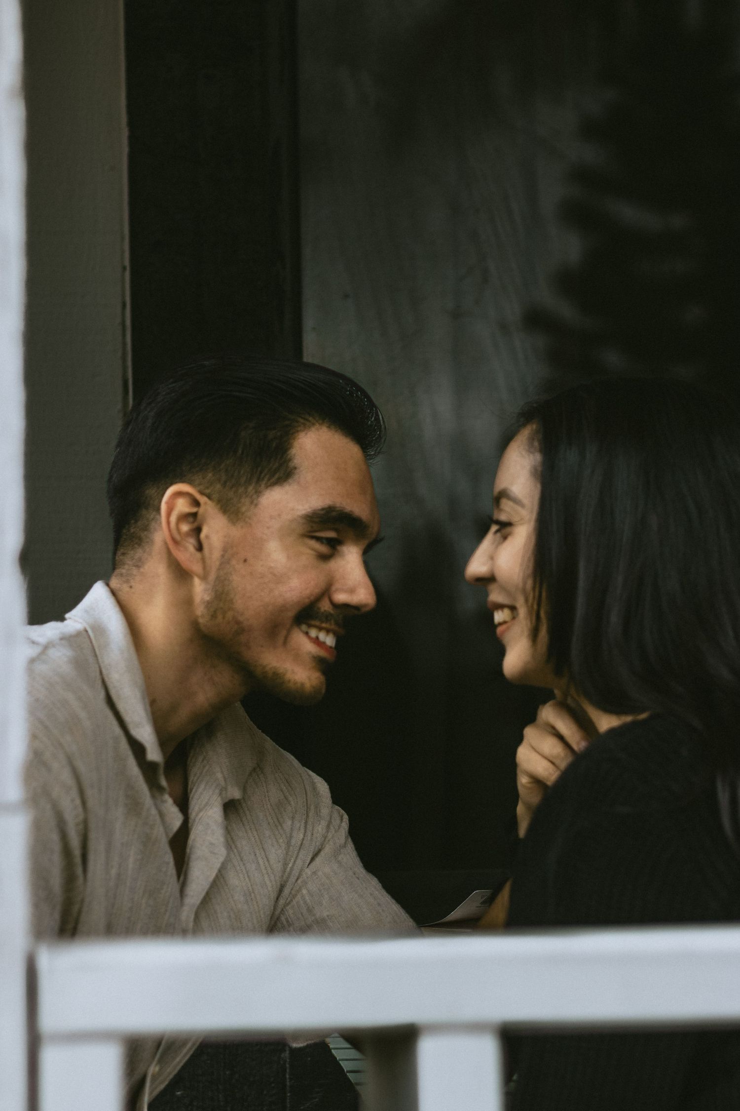Couple sharing an intimate moment while looking at each other through a window frame.