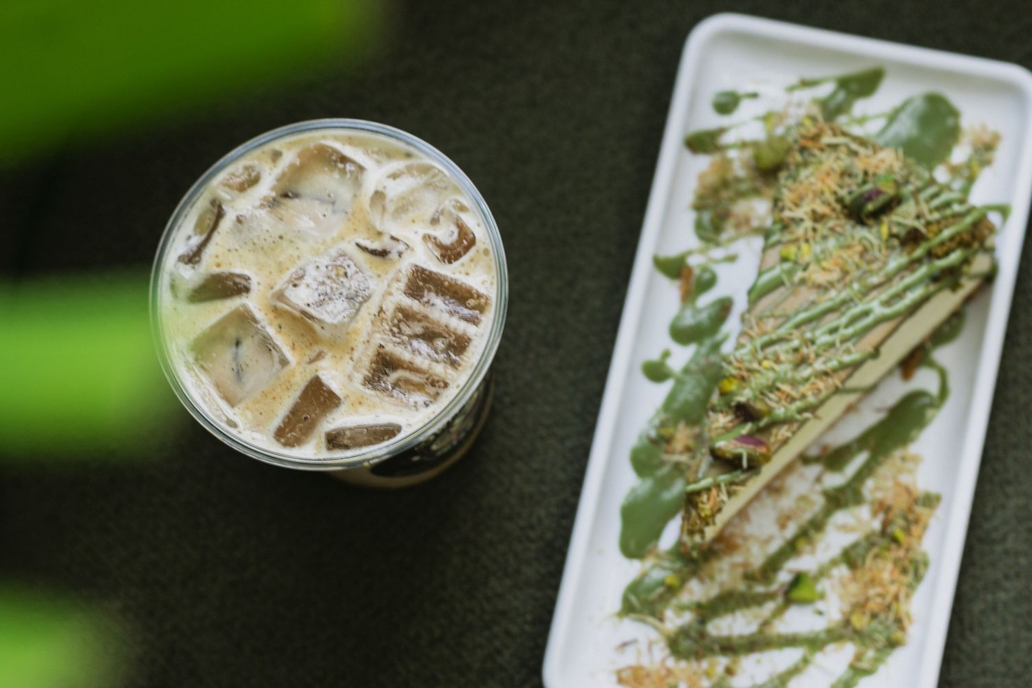 A refreshing iced beverage served alongside a white plate with drizzled sauce and crunchy toppings.