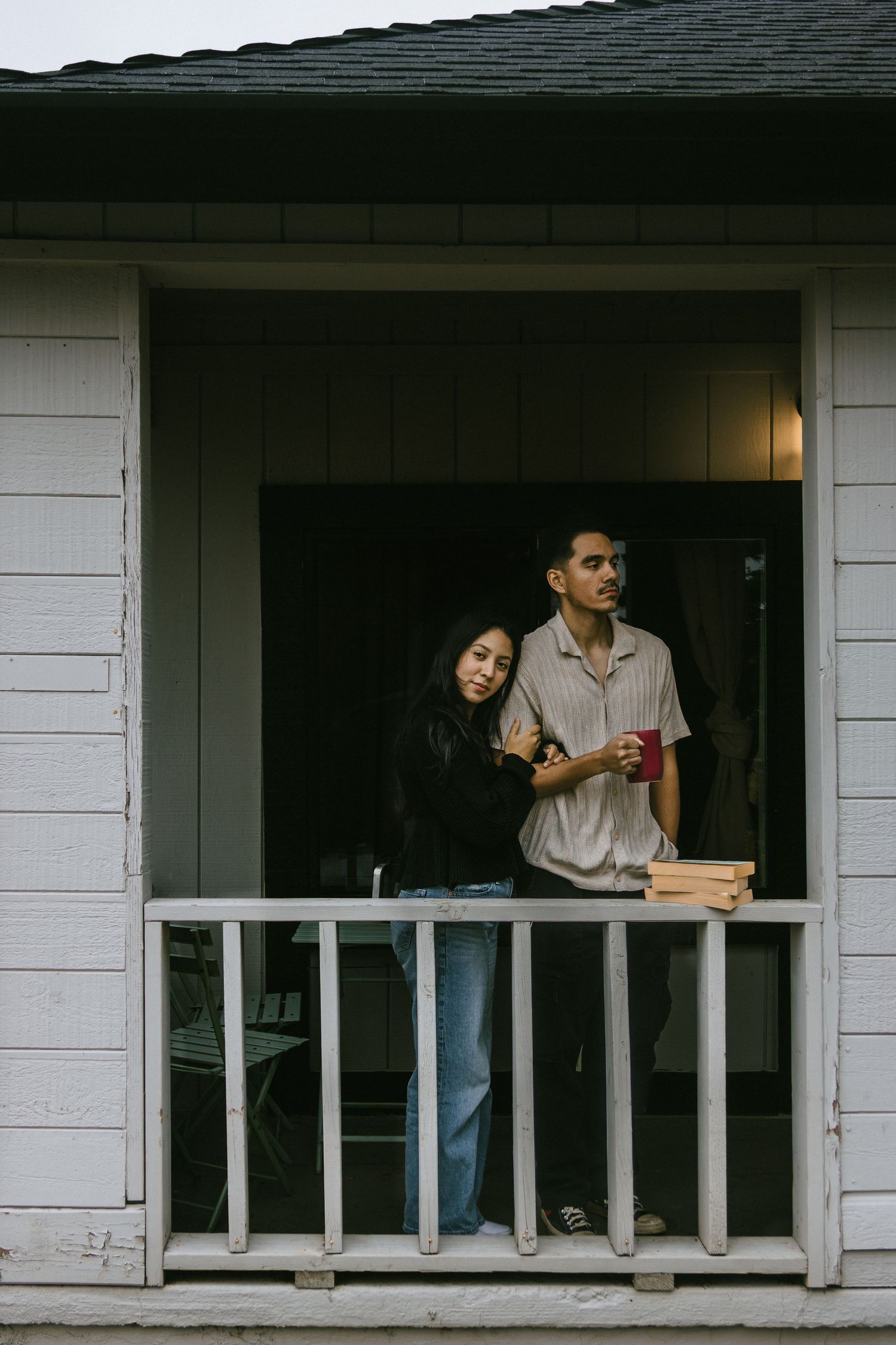 Two people sitting on white porch railing with books and drinks.