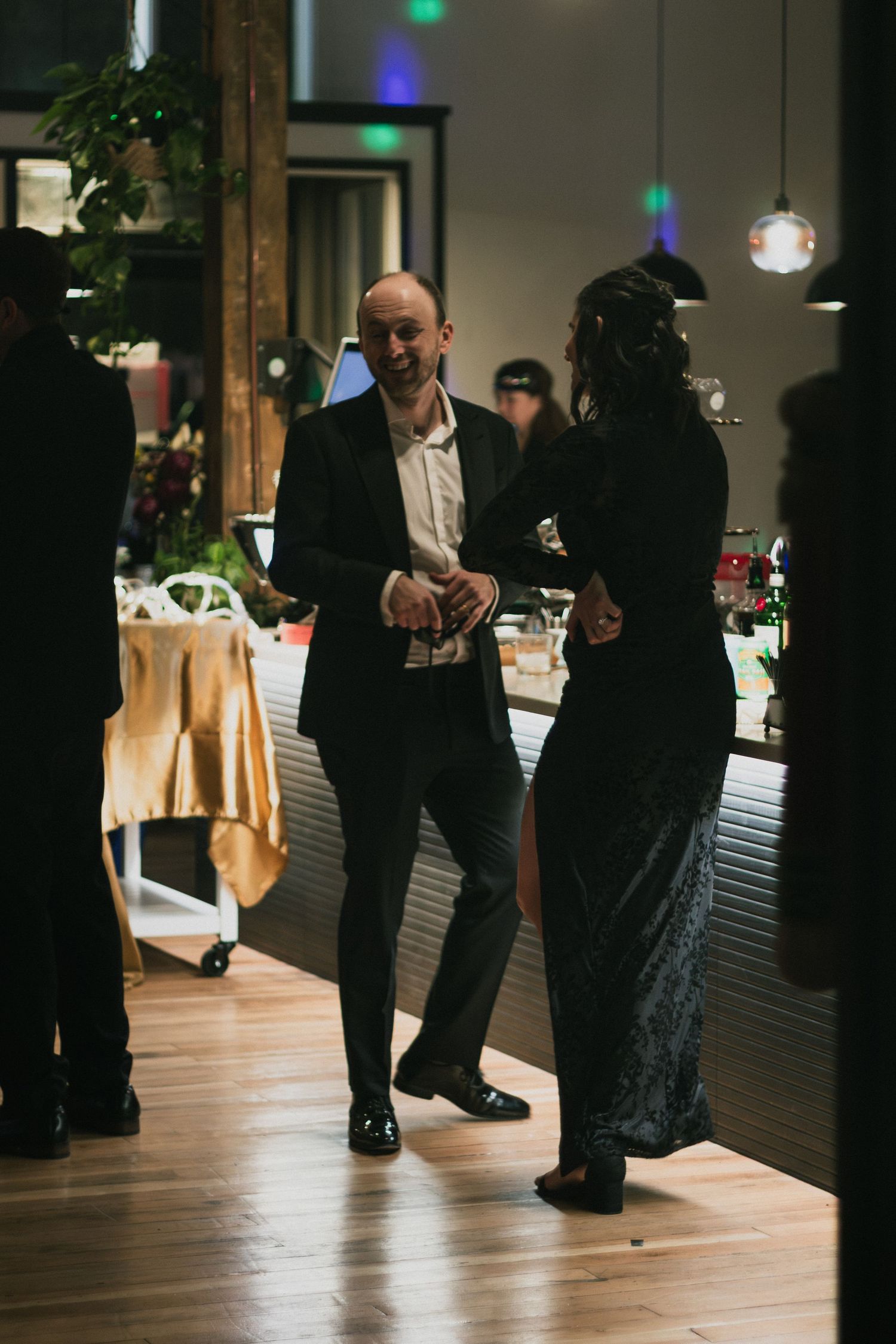 Couple dancing together at upscale indoor event venue with decorative lighting and buffet table nearby.