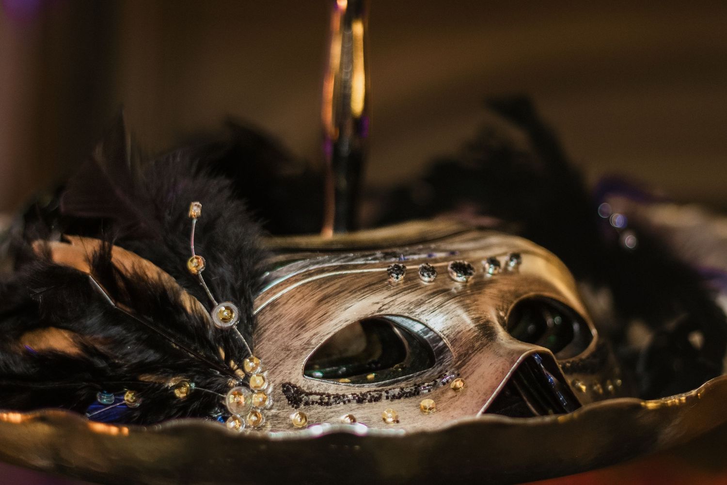 Ornate gold and black Venetian masquerade mask adorned with feathers and jewels on a dark background.