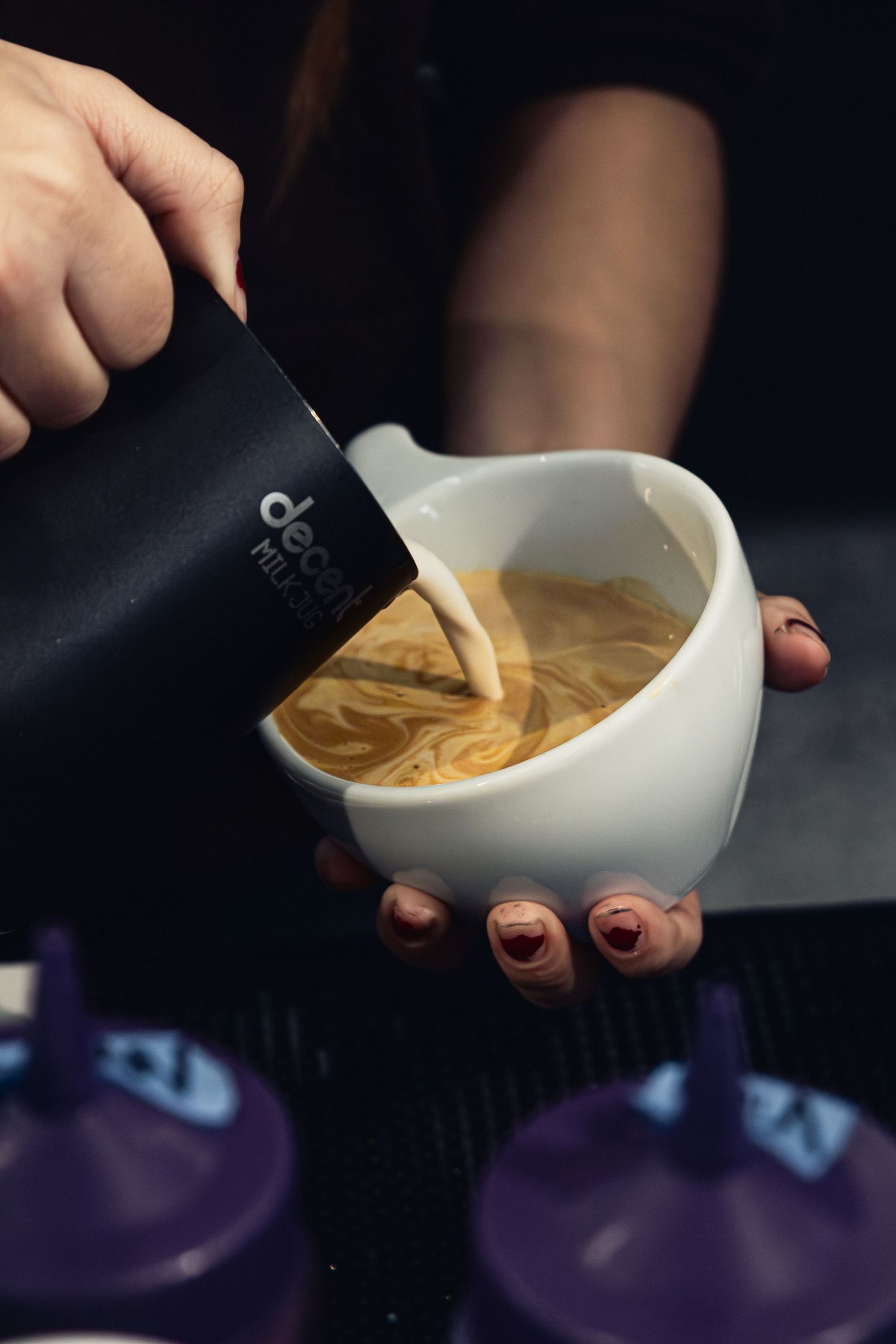 Hands pouring steamed milk in circular motion to create latte art pattern.