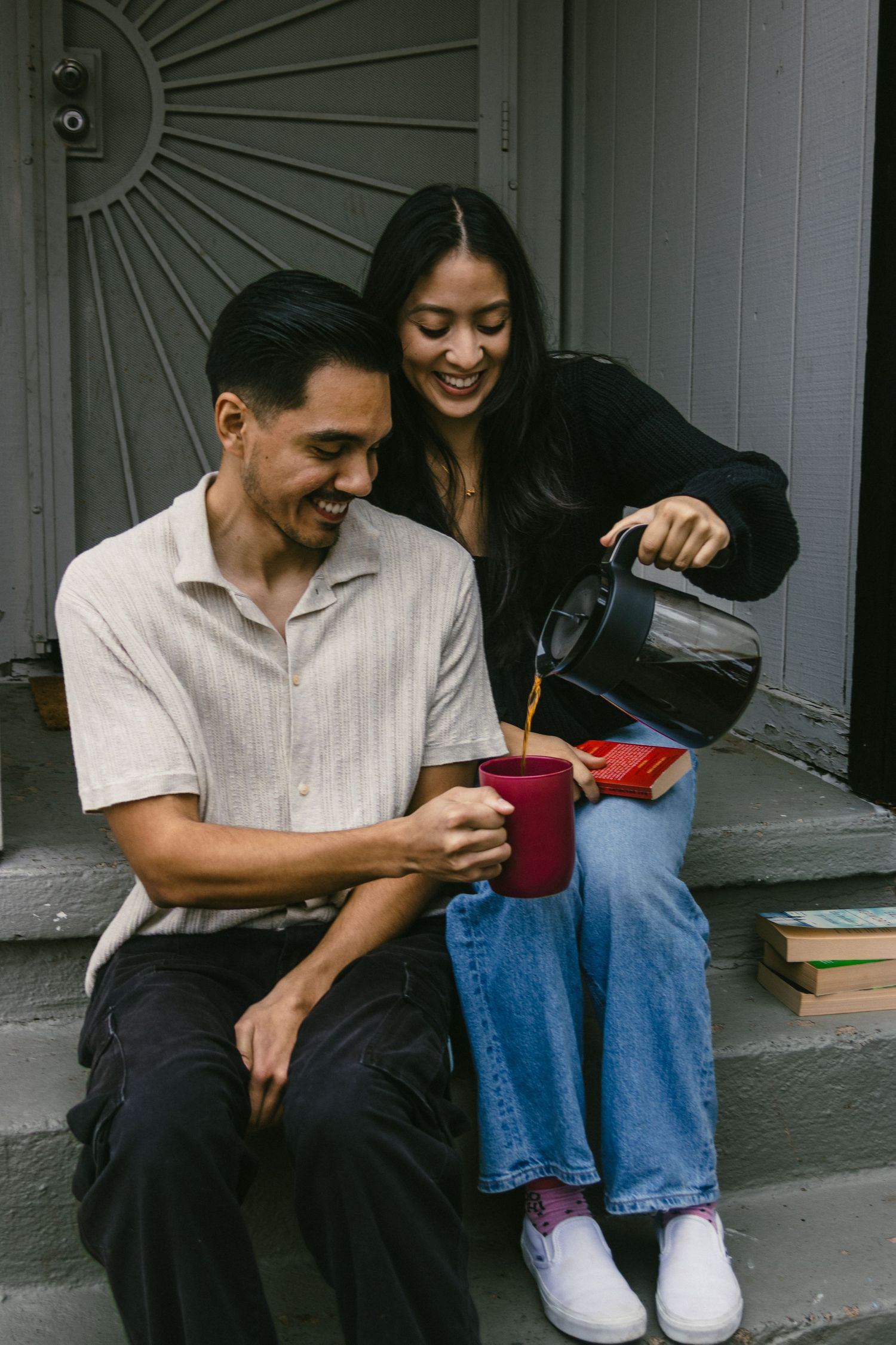 Friends sharing laughter while enjoying coffee and books on outdoor steps.