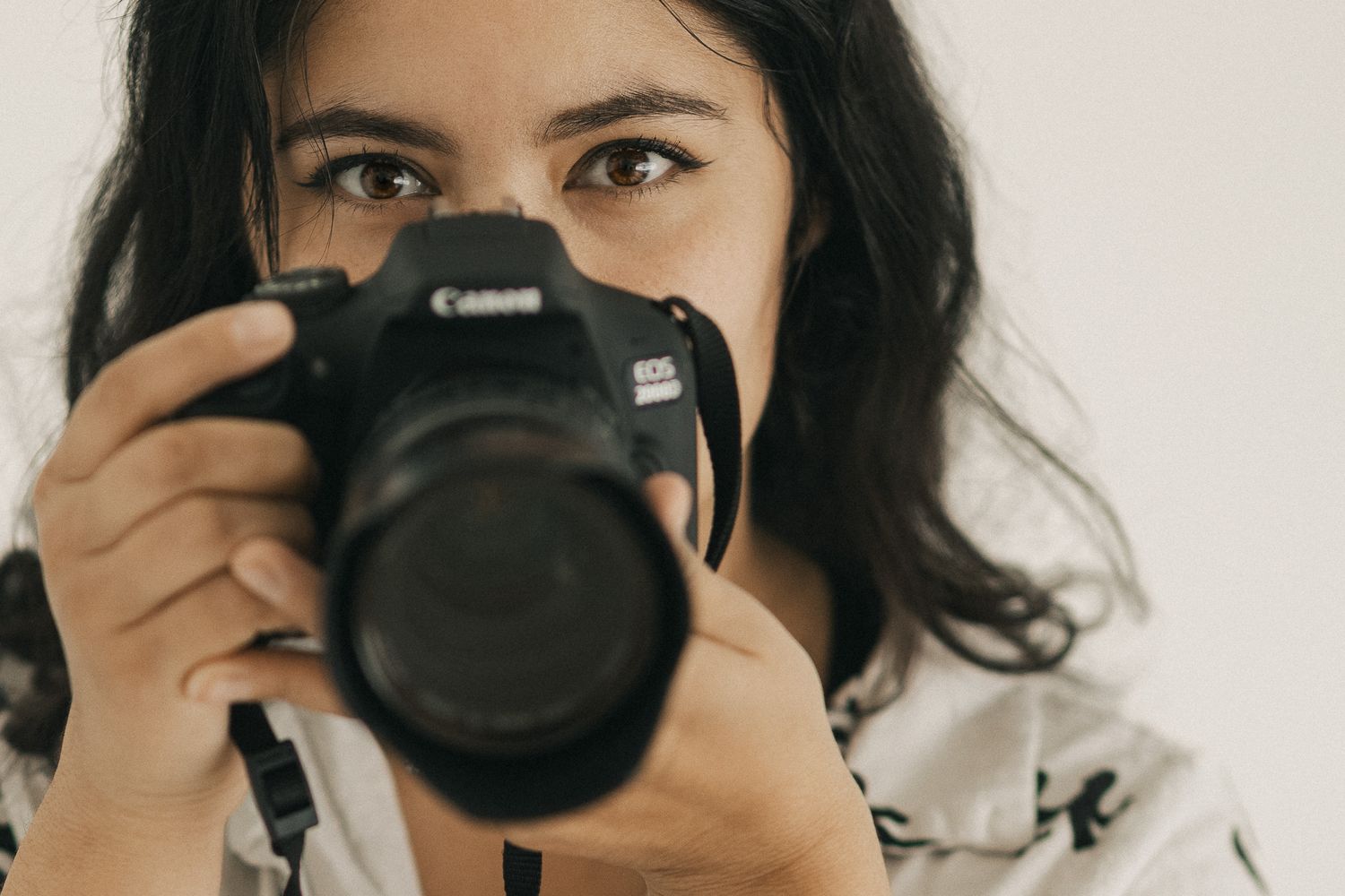 A person holding a black Canon DSLR camera takes a self-portrait in a mirror reflection.