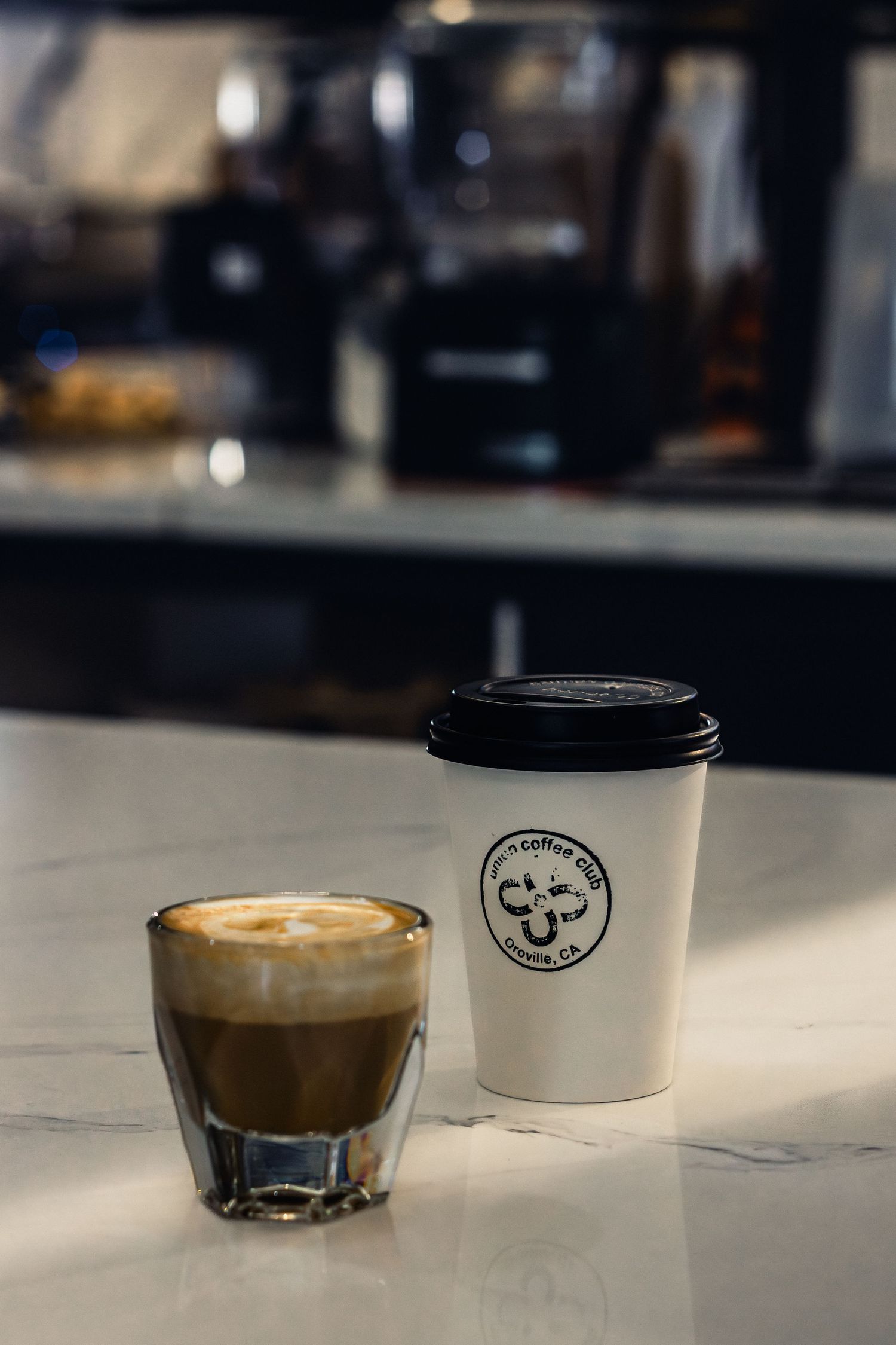 Coffee drinks and branded takeaway cups arranged on marble counter in cafe setting.
