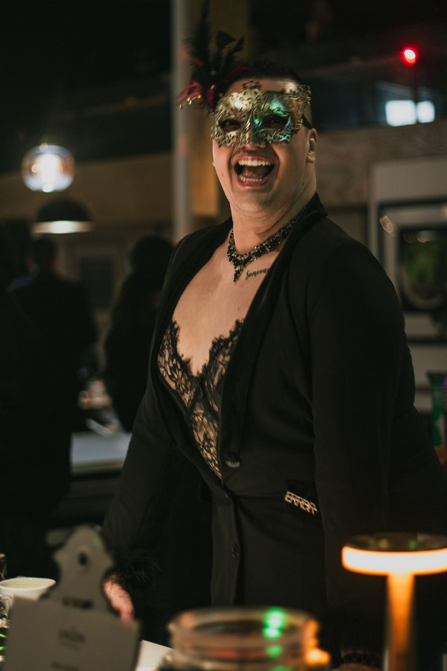 Person laughing at masquerade party wearing gold mask and black lace outfit.