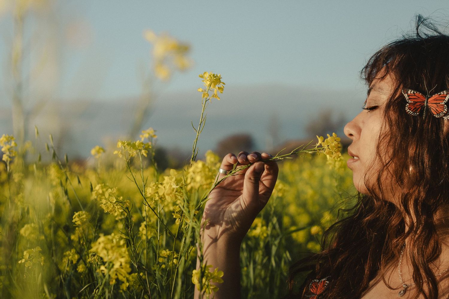 Artistic portraits in a golden mustard flower field during sunset with butterfly sunglasses.