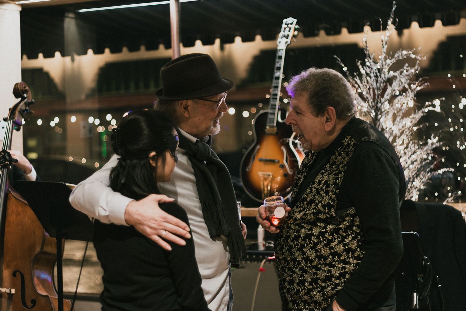 Musician in black hat embraces guest at elegant evening event with instruments visible in background.