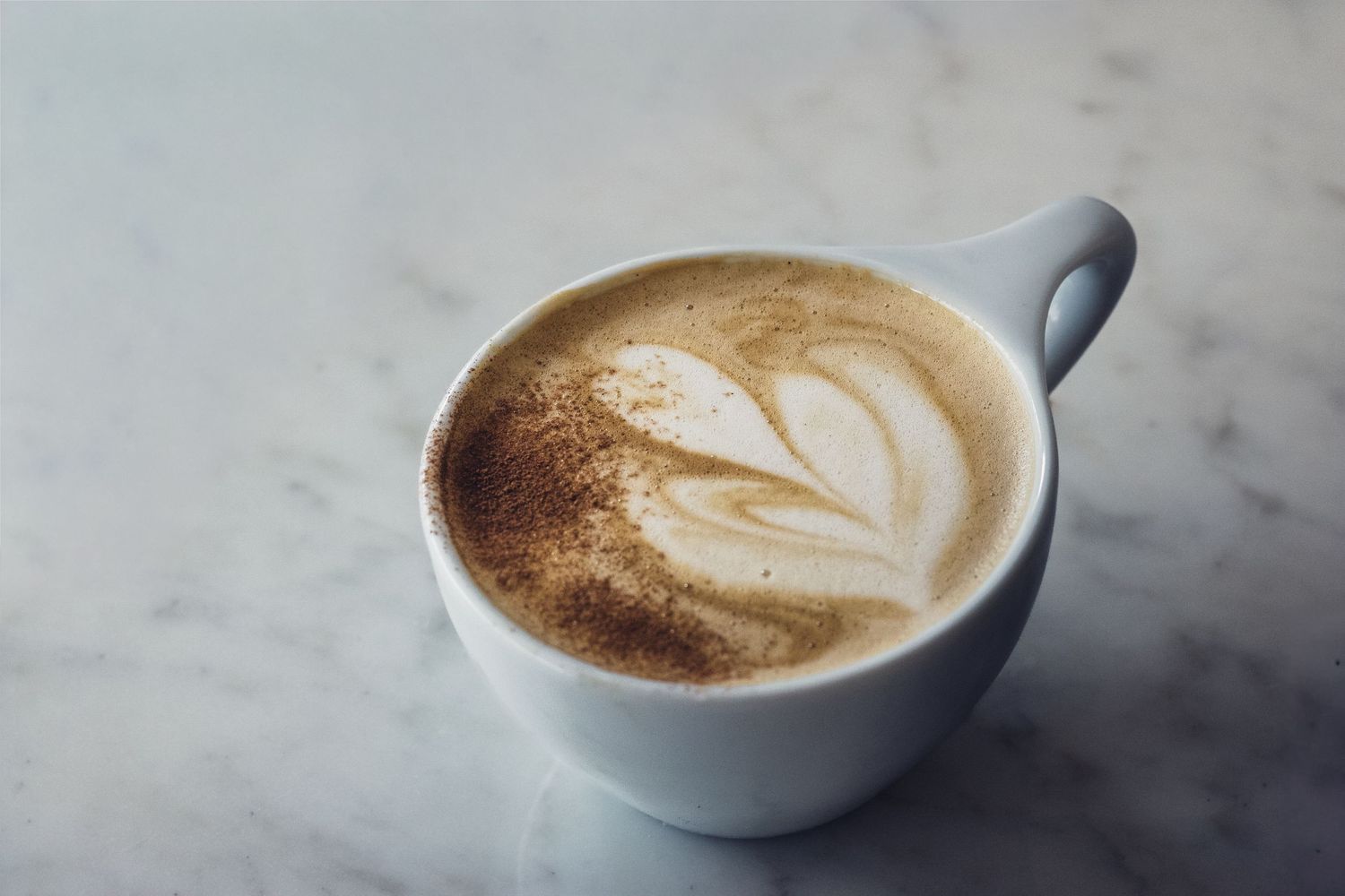 White ceramic cup containing latte with delicate leaf art pattern.