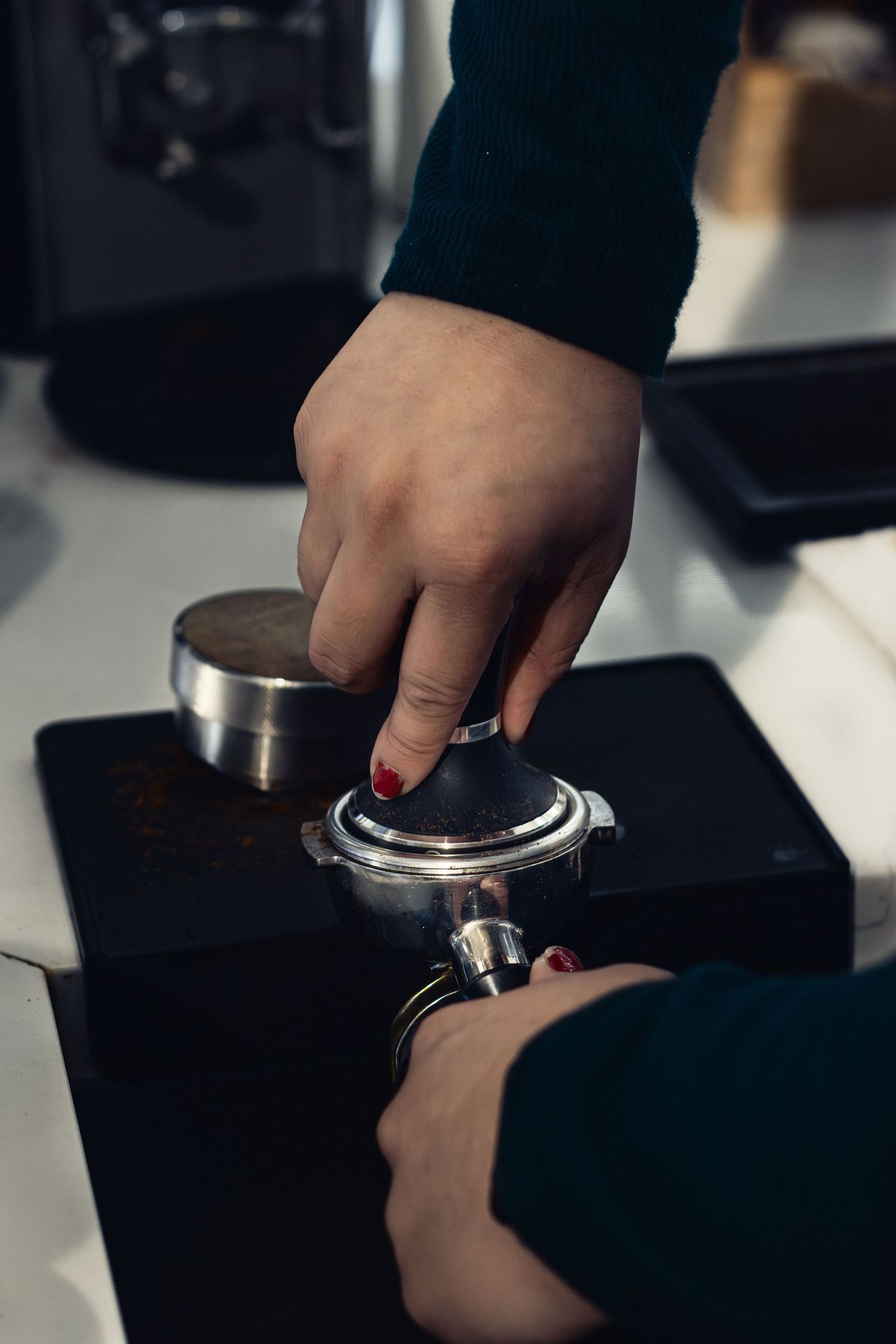 Hands tamping coffee grounds into a portafilter on an espresso machine.