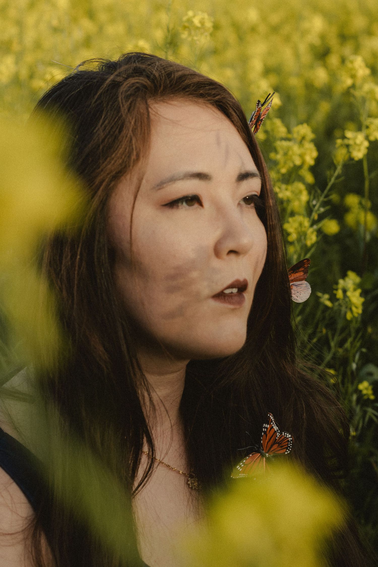 A dreamy portrait in a yellow flower field with a monarch butterfly creating a whimsical natural scene.