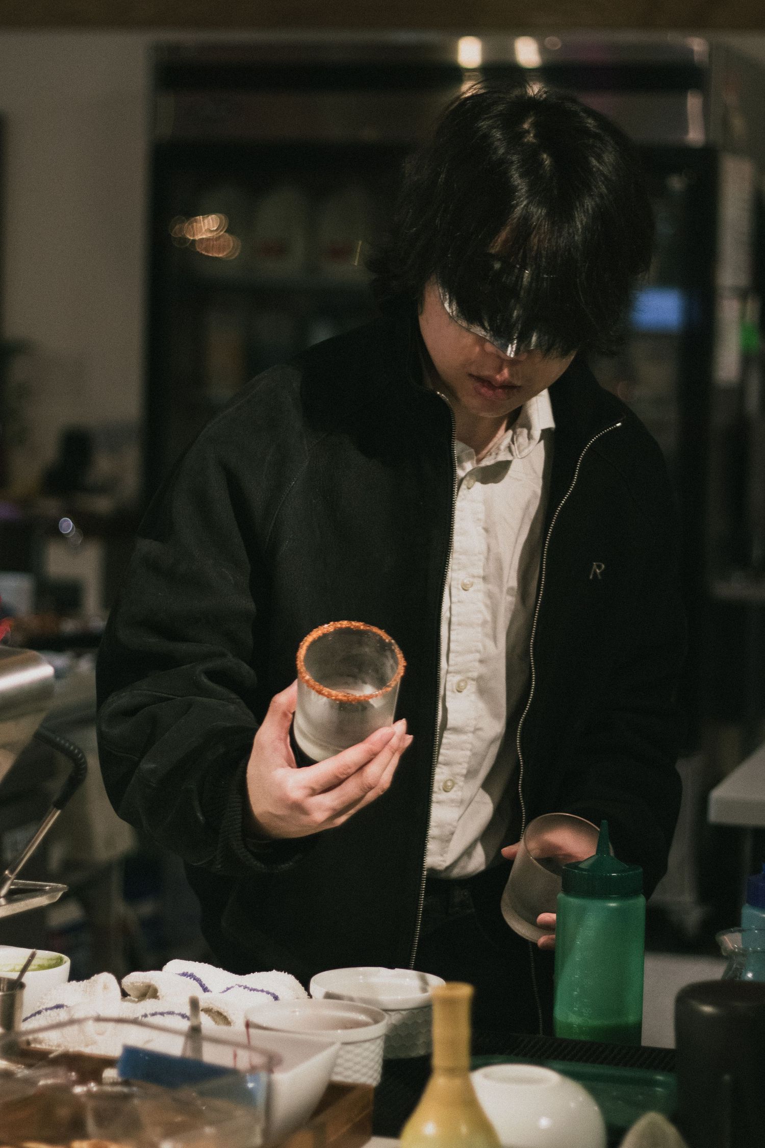 Young man in black jacket examining ceramic cup at pottery display table.