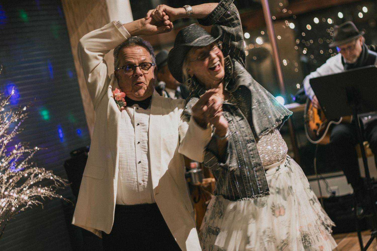 Couple dancing joyfully at a wedding reception with a live band performing in the background.
