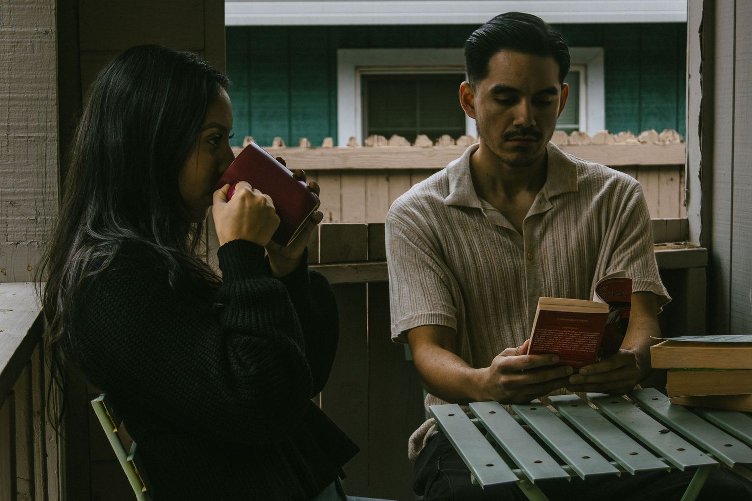 Couple relaxing on porch with coffee mugs and books in moody lighting.