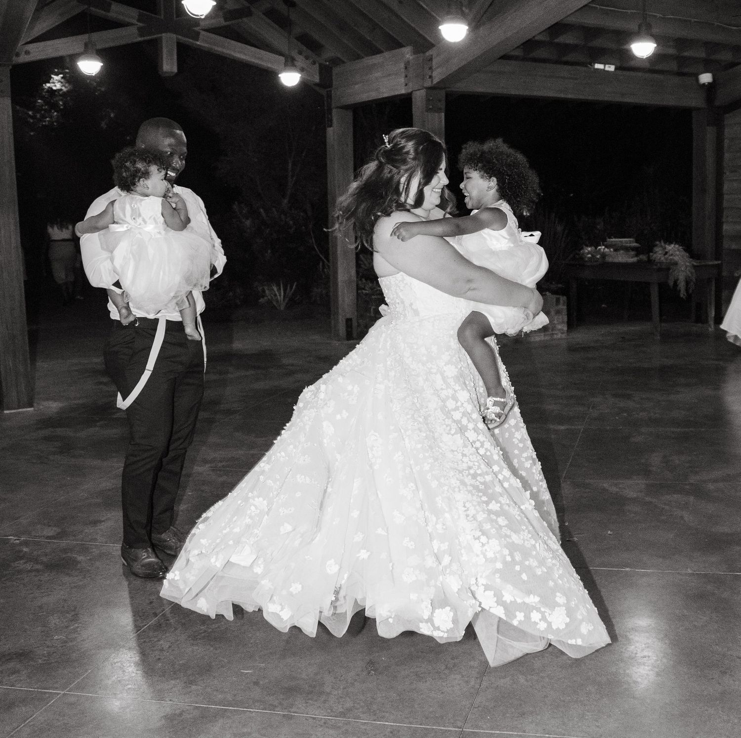 Black and white photo of bride and groom dancing with children at their wedding reception.