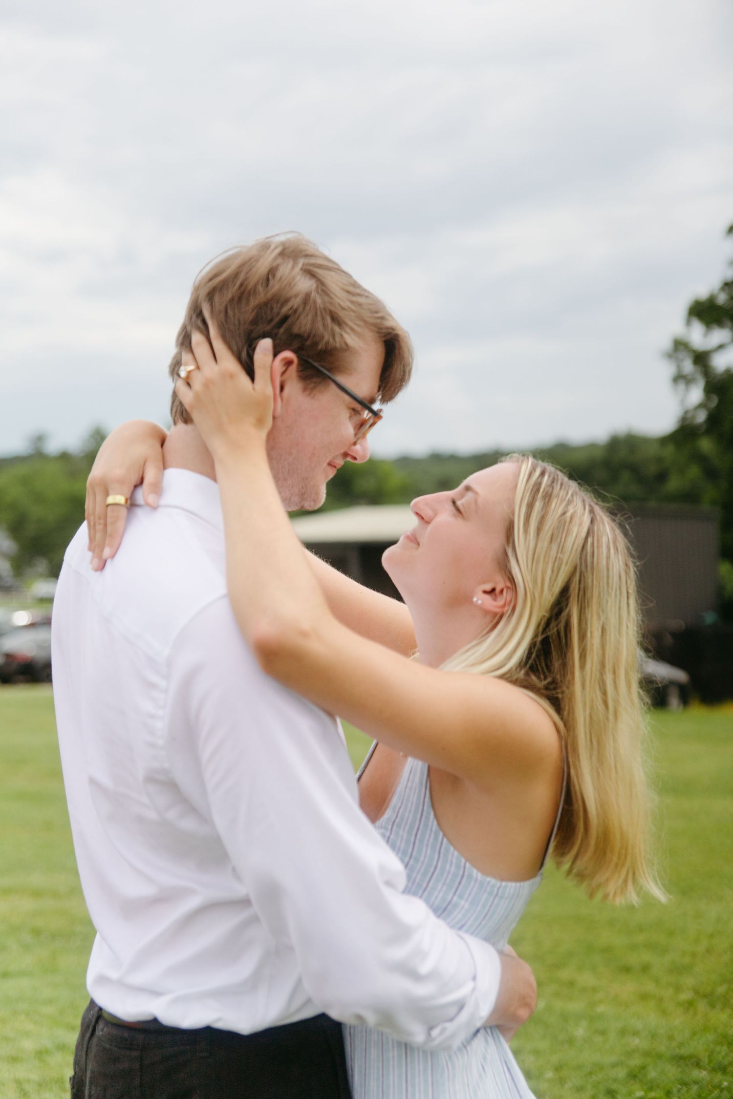 Happy couple embracing and laughing together during outdoor engagement photos on green lawn.