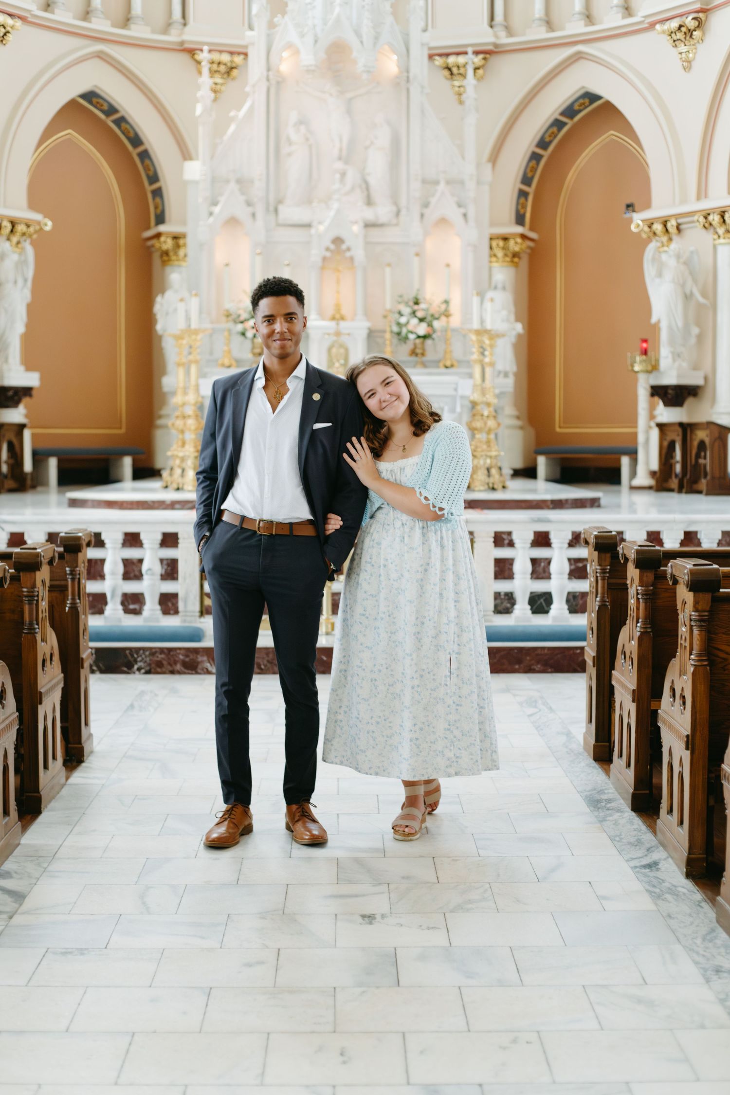 Interracial couple posing together in an elegant church aisle with ornate arches and marble floors.