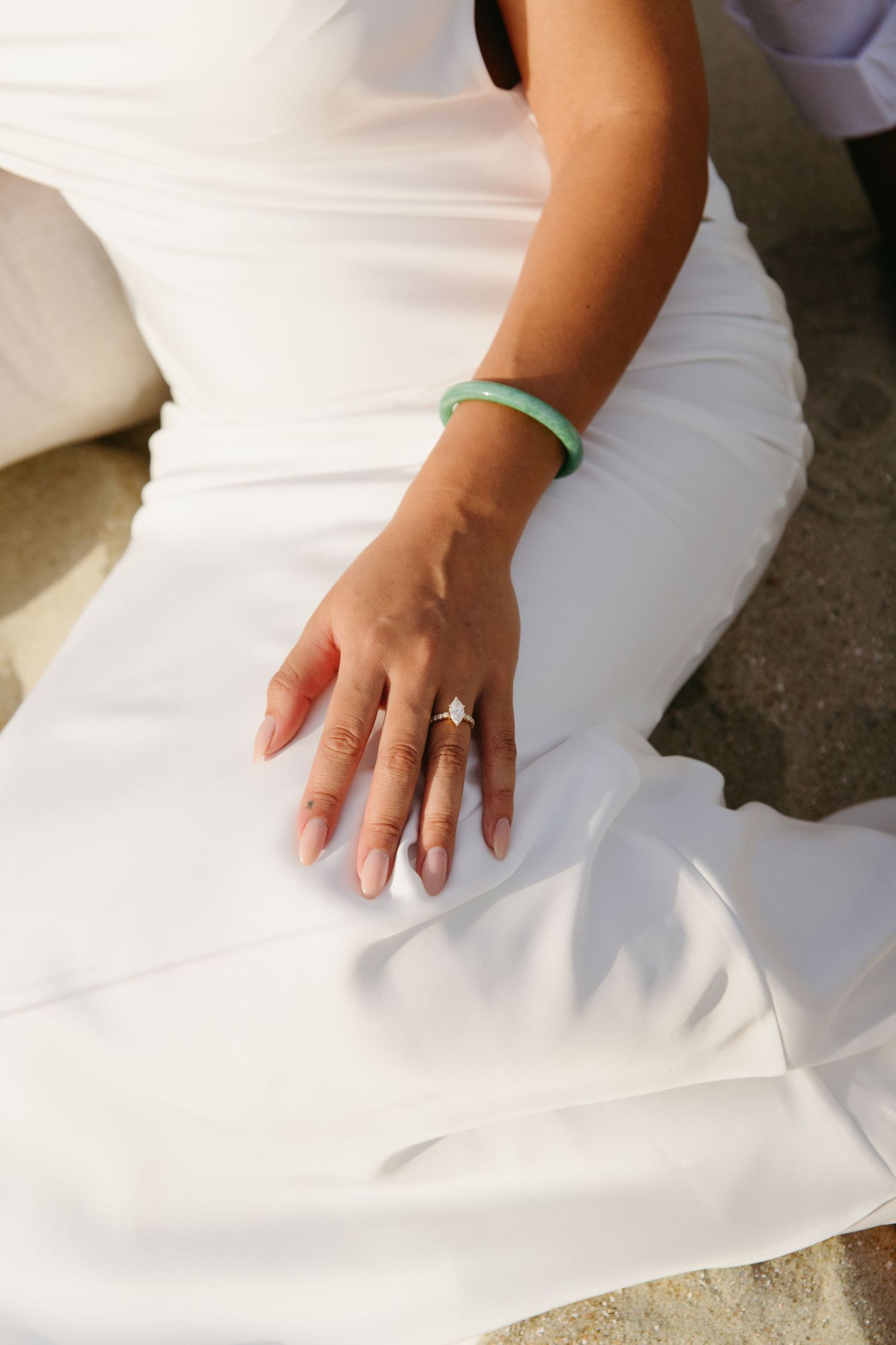 Bride in white dress displaying star-shaped engagement ring and green jade bracelet.