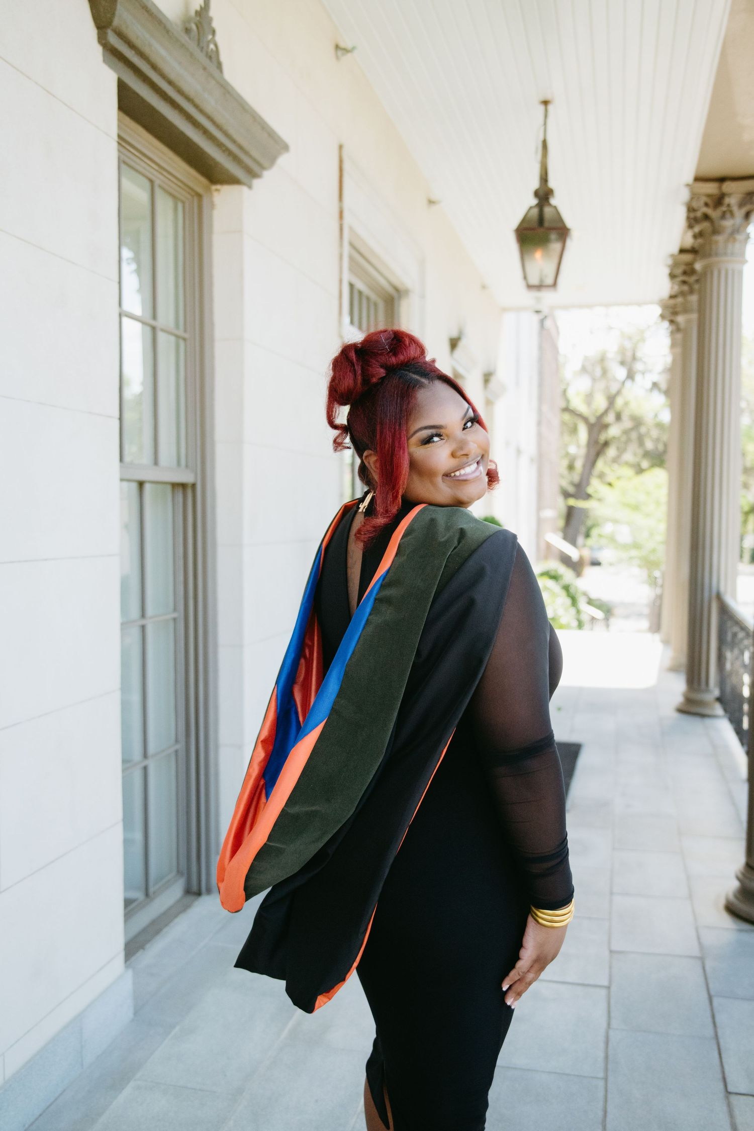 Black woman in black dress with colorful graduation stole smiling over shoulder.