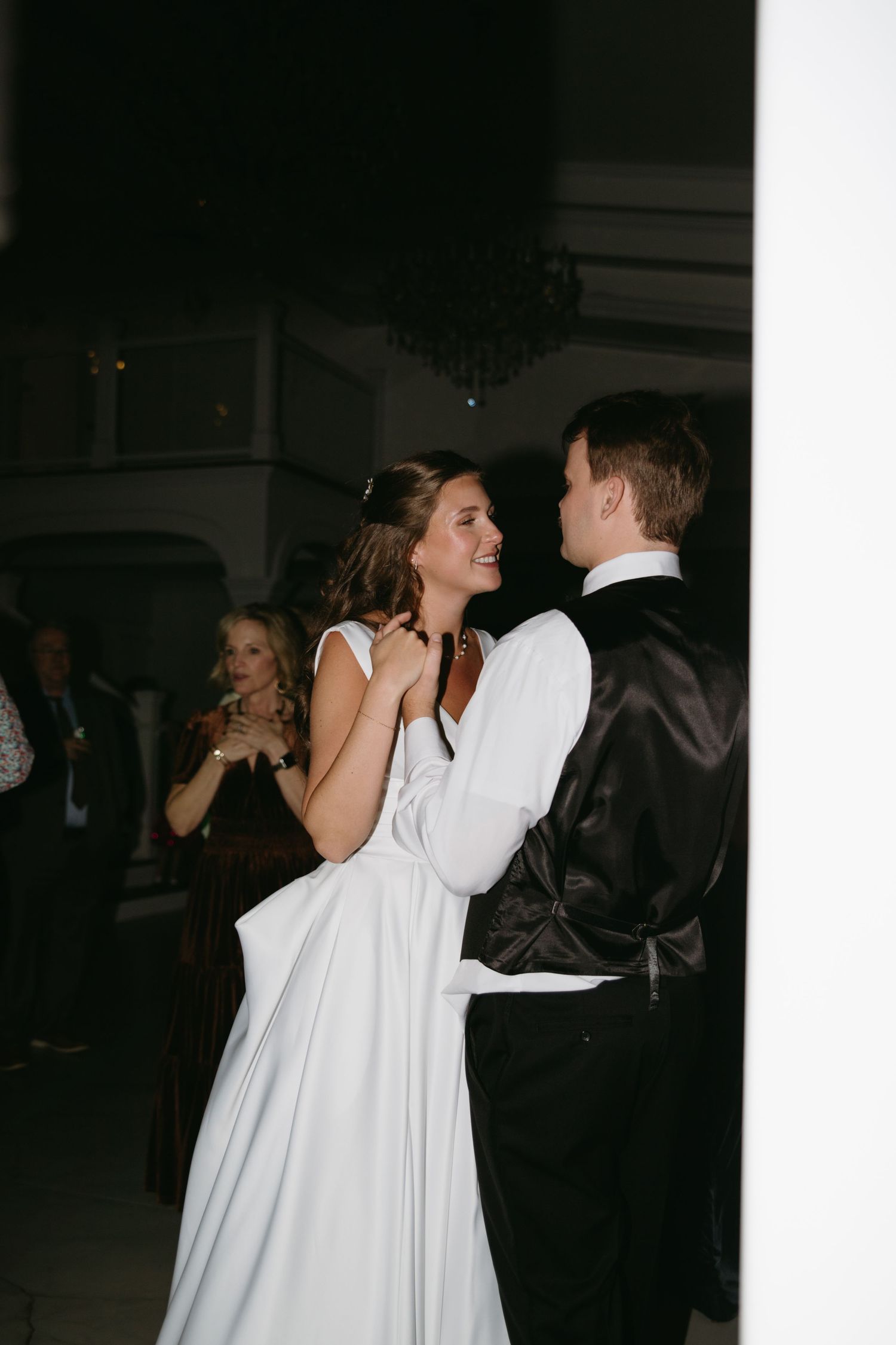 Bride in white gown smiling during first dance with groom at elegant wedding reception.