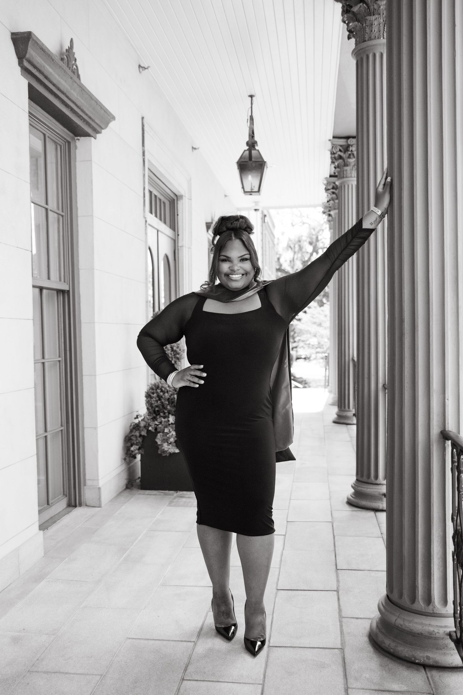 Woman in black dress poses elegantly between white columns in black and white portrait photography.