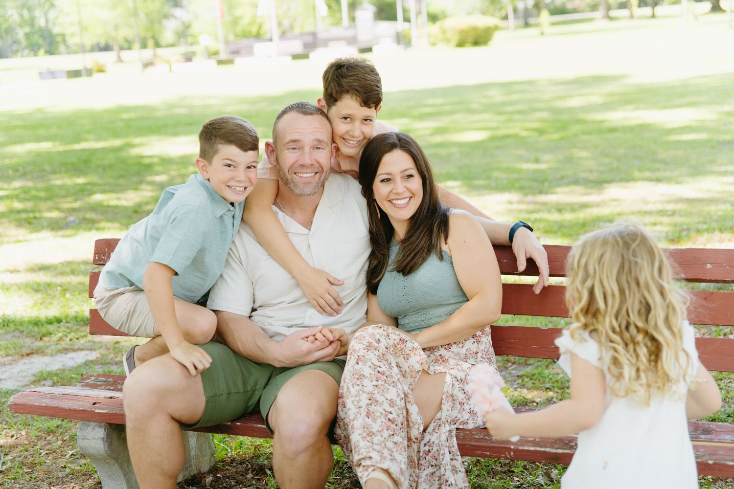 Happy family of five sitting together on red park bench smiling outdoors.
