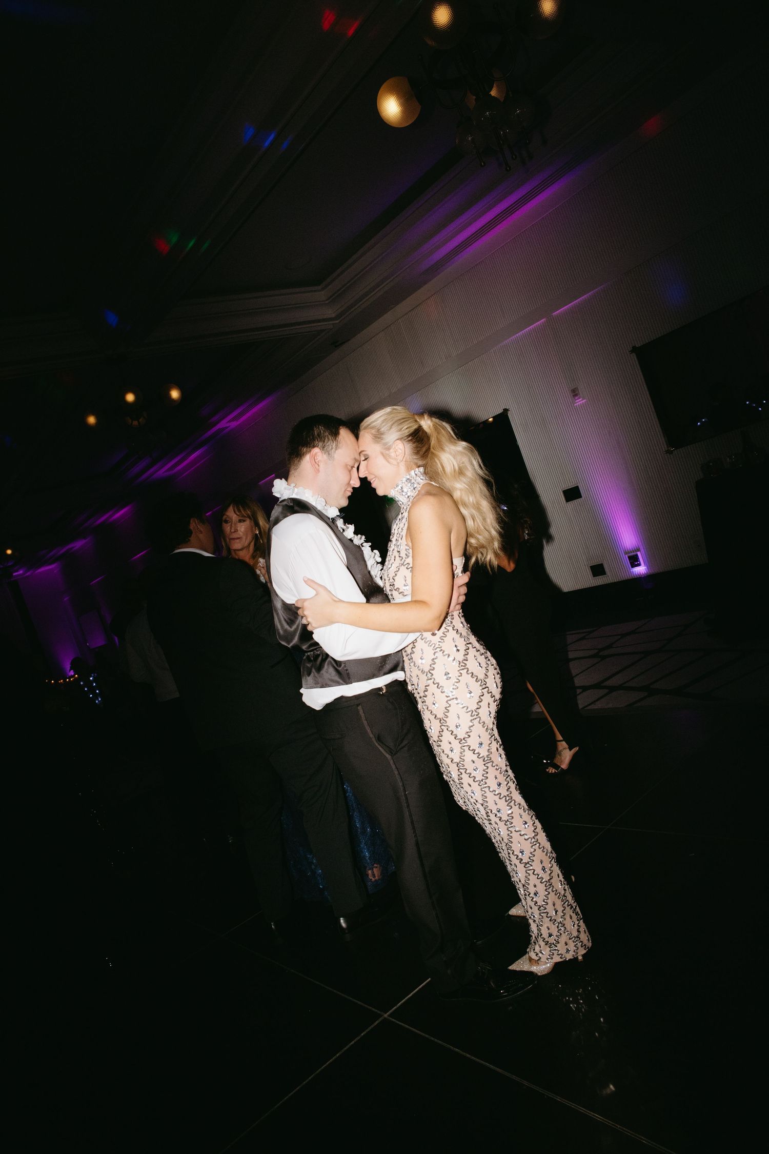 Bride and groom sharing intimate first dance in dimly lit ballroom with purple uplighting.