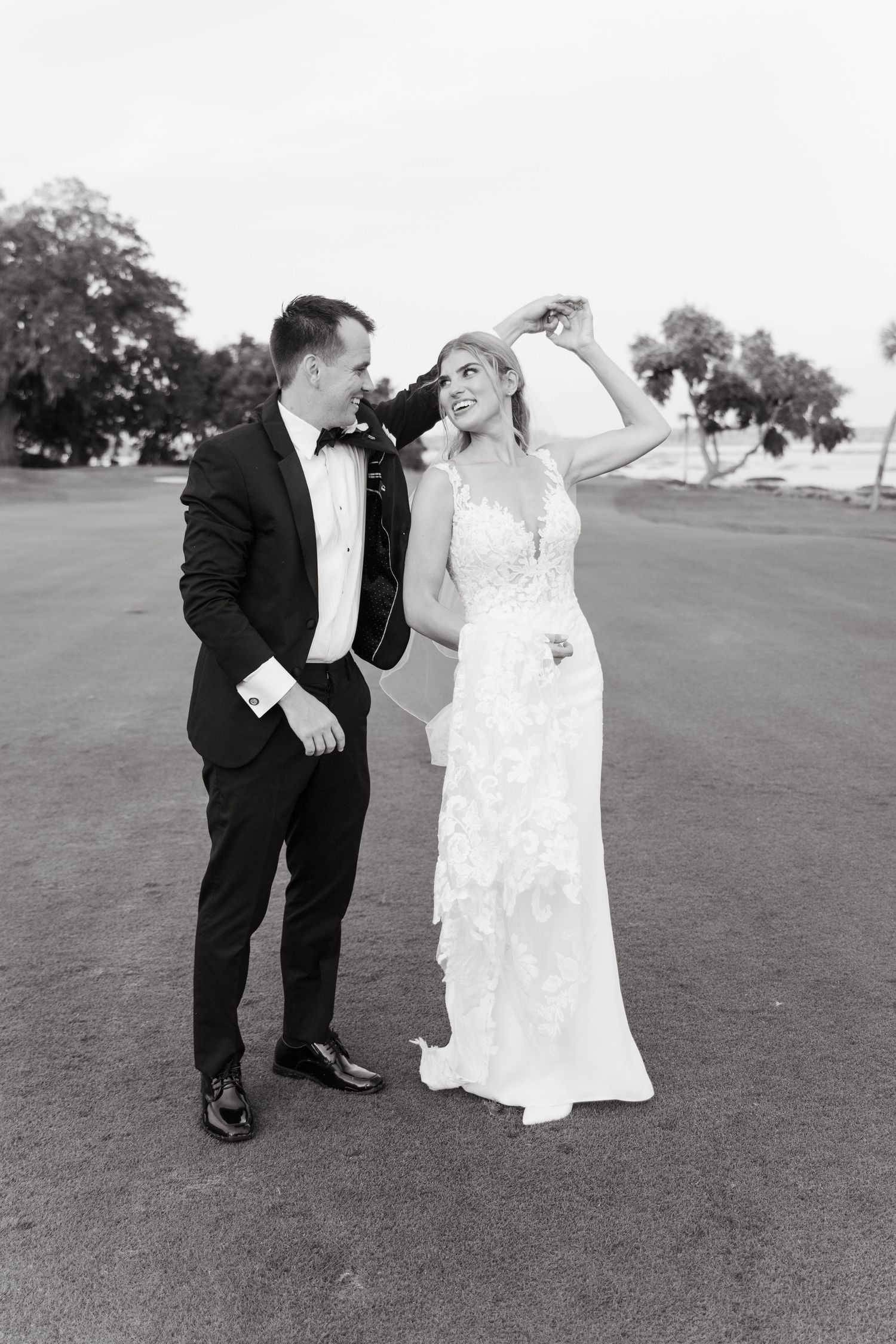 Black and white photo of bride and groom dancing on a golf course, bride in lace gown.
