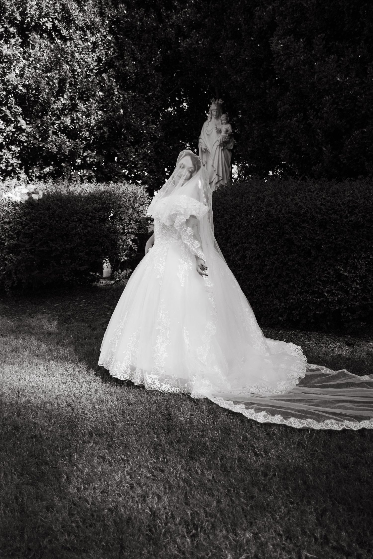 Bride in a voluminous lace wedding gown with a long veil walking through a manicured garden.