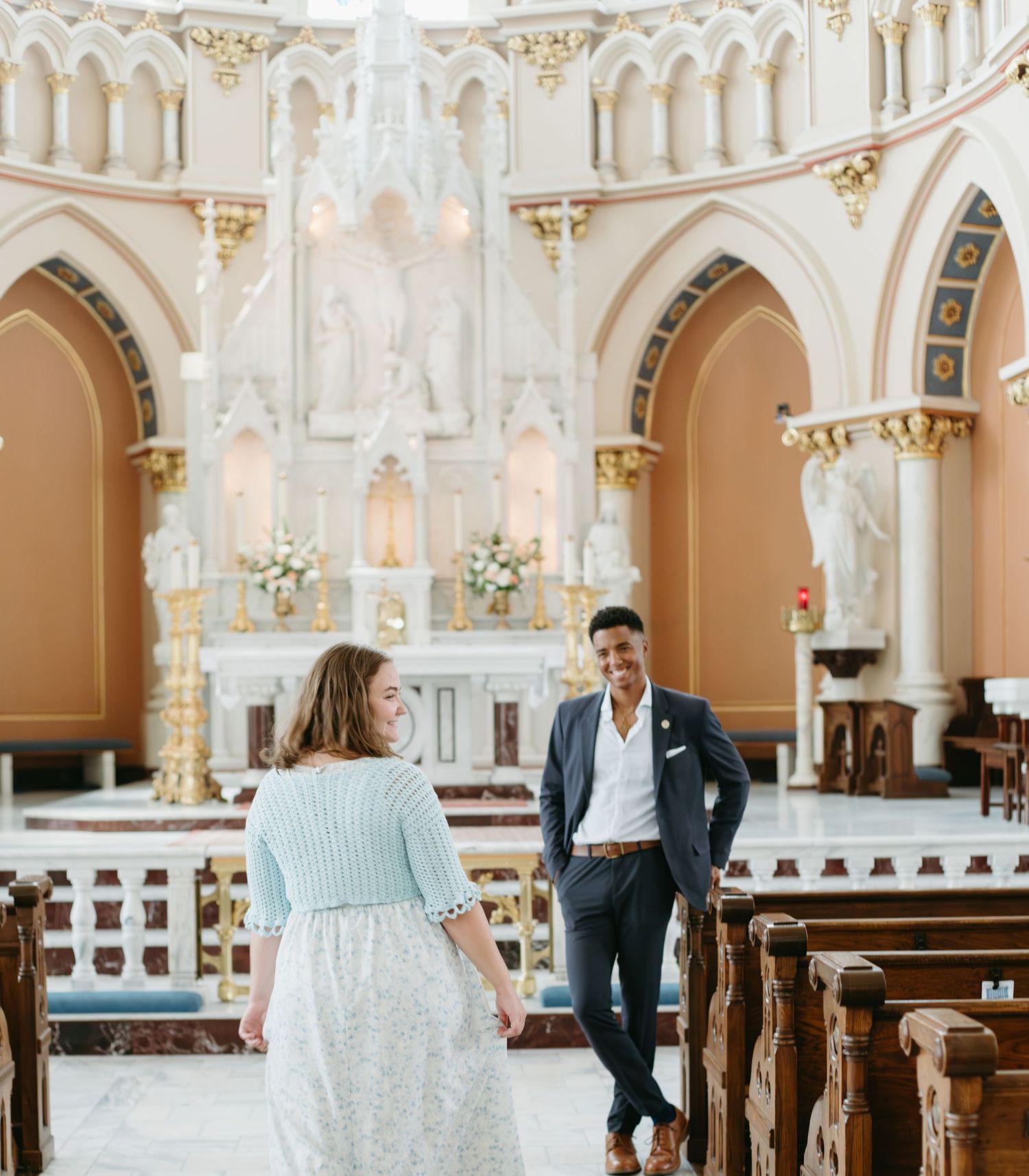 Couple holding hands in stunning ornate white cathedral with gothic arches and golden altar details.