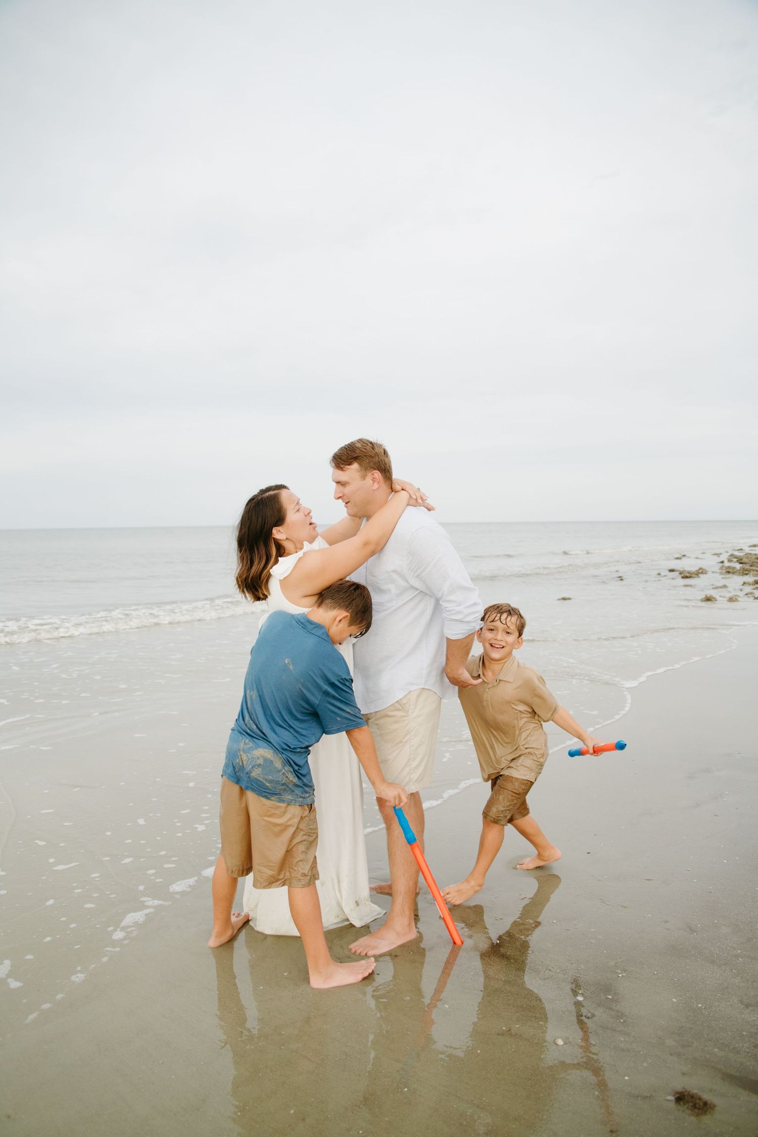 Family of four plays together in ocean waves on an overcast beach day.