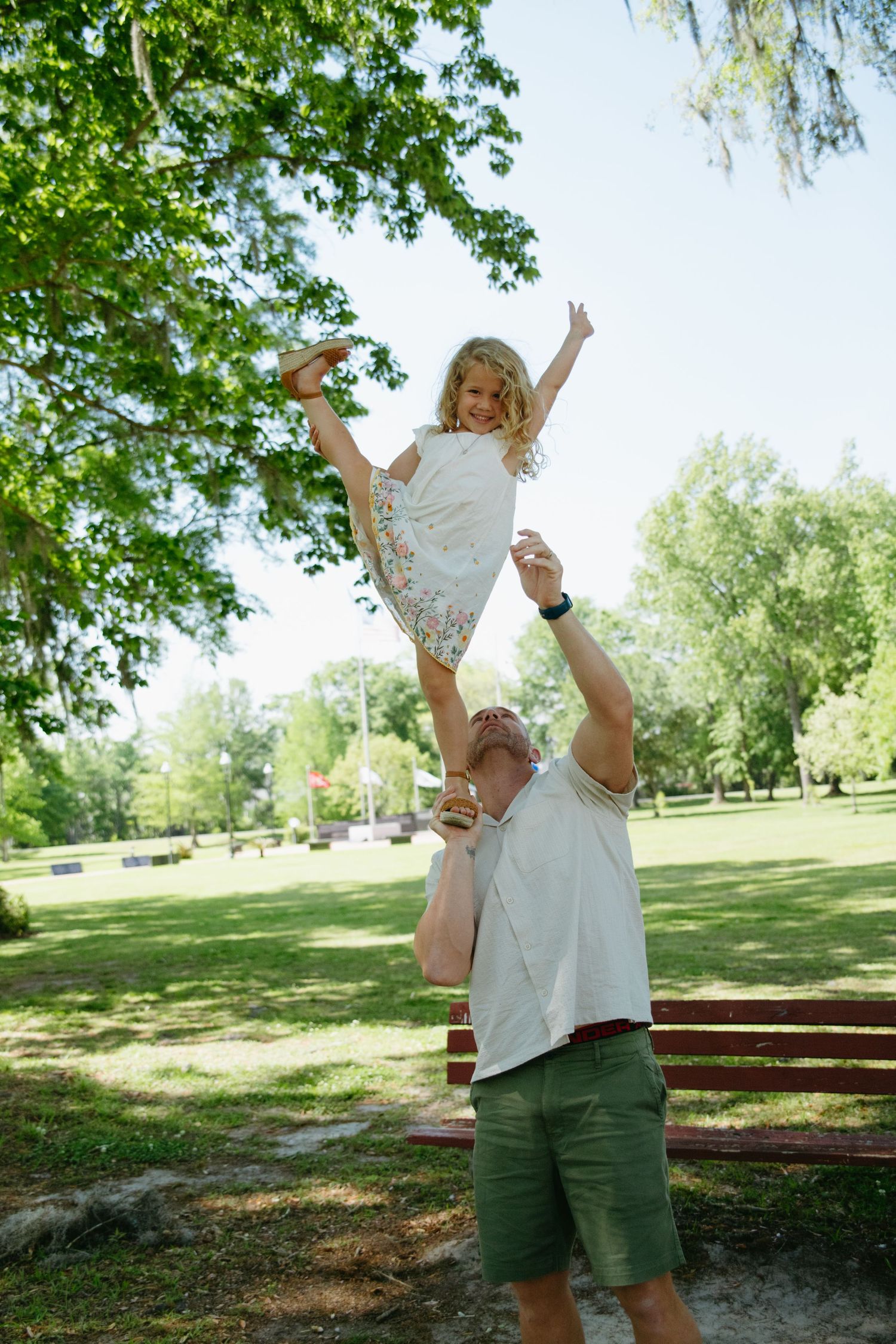 Father lifting young daughter overhead in sunny green park, joyful family moment outdoors.