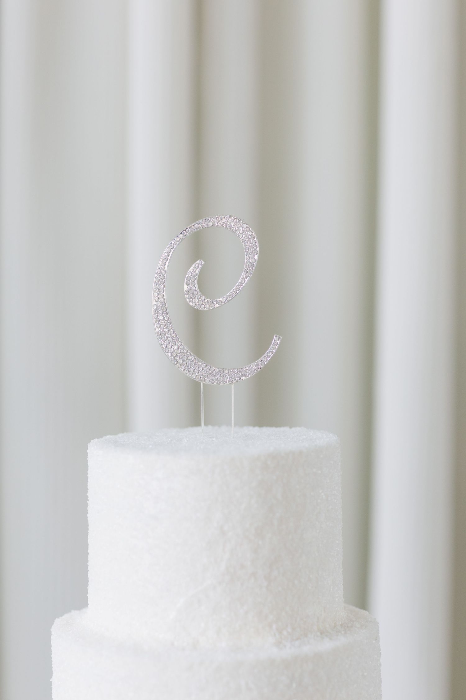 White wedding cake topped with crystal rhinestone letter C monogram cake topper.
