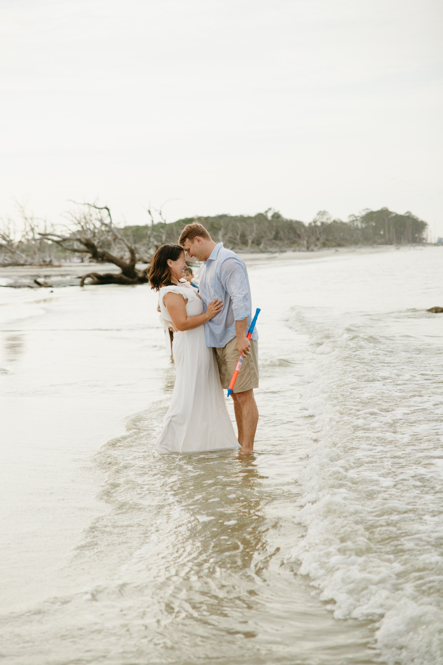 Couple sharing a romantic kiss while standing in ocean waves on a sandy beach during golden hour.