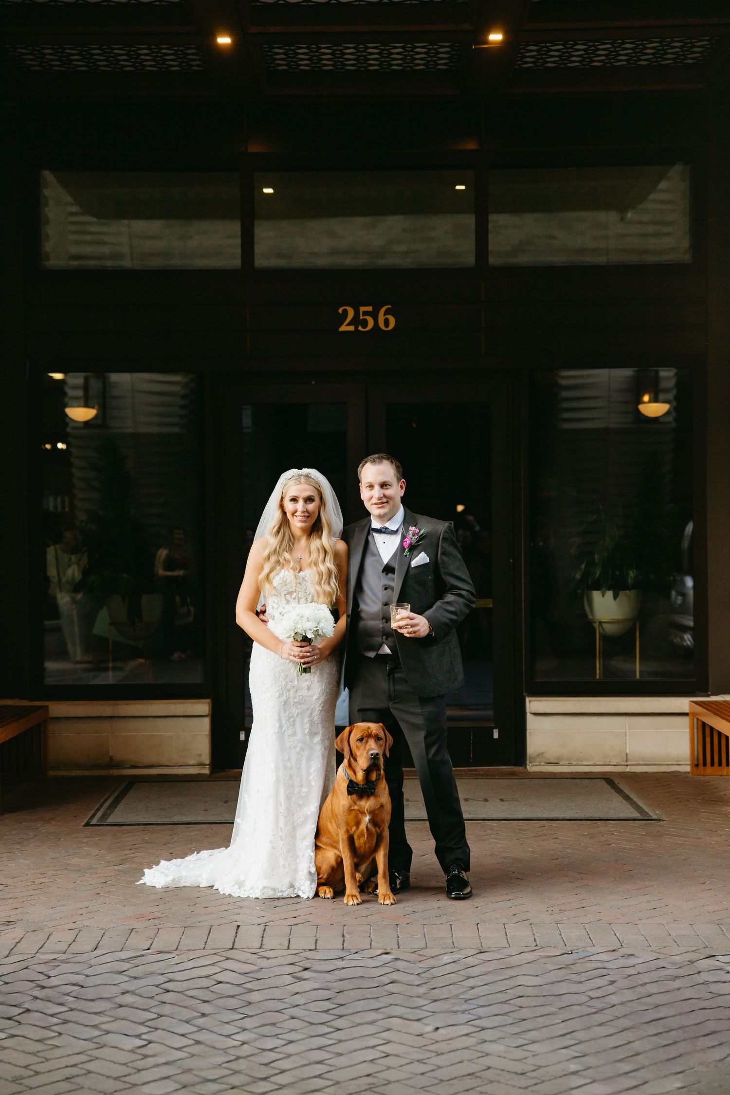 Bride and groom posing with their brown dog in front of building number 256 entrance.