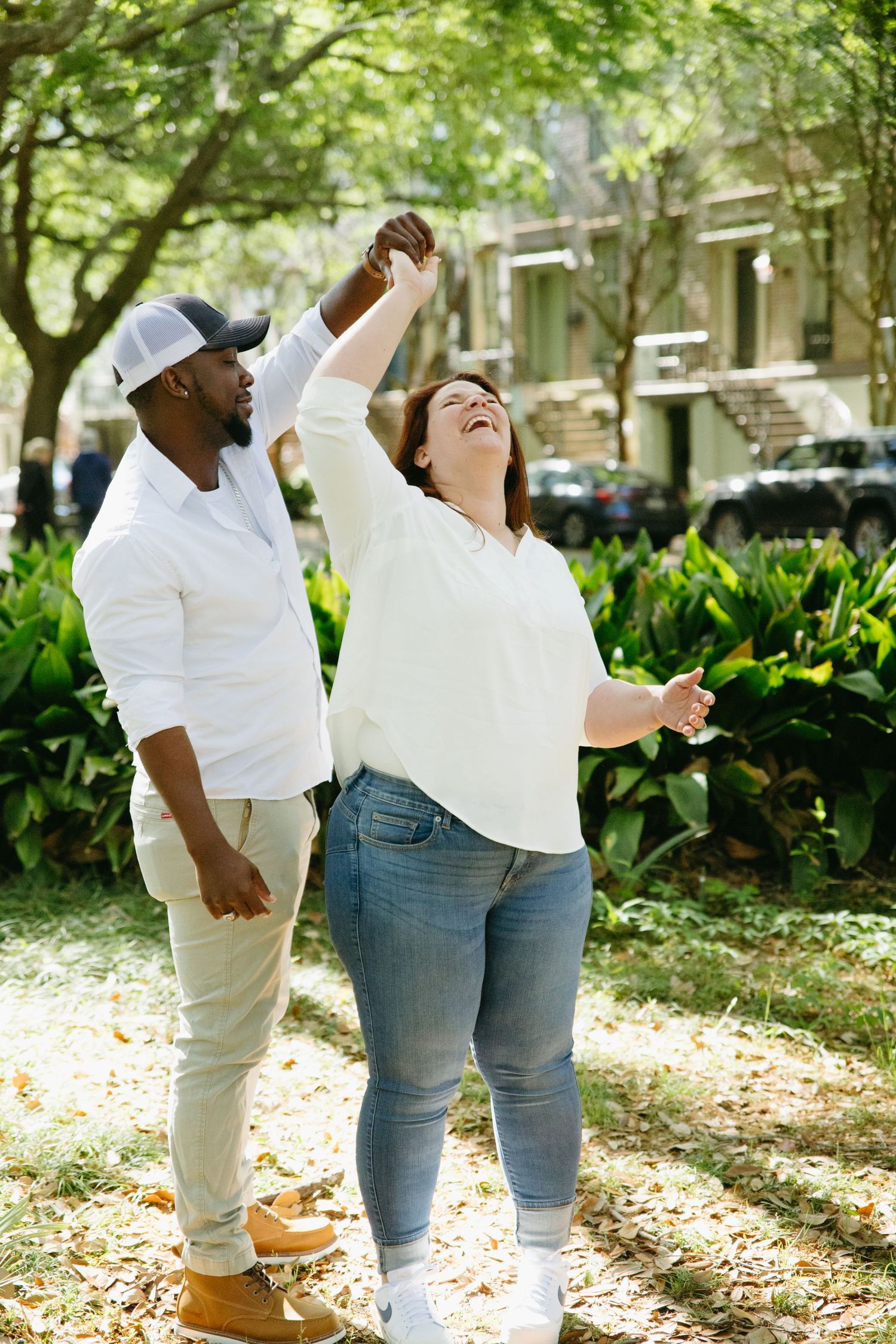 Joyful interracial couple dancing outdoors in a lush green park, woman laughing as man spins her.