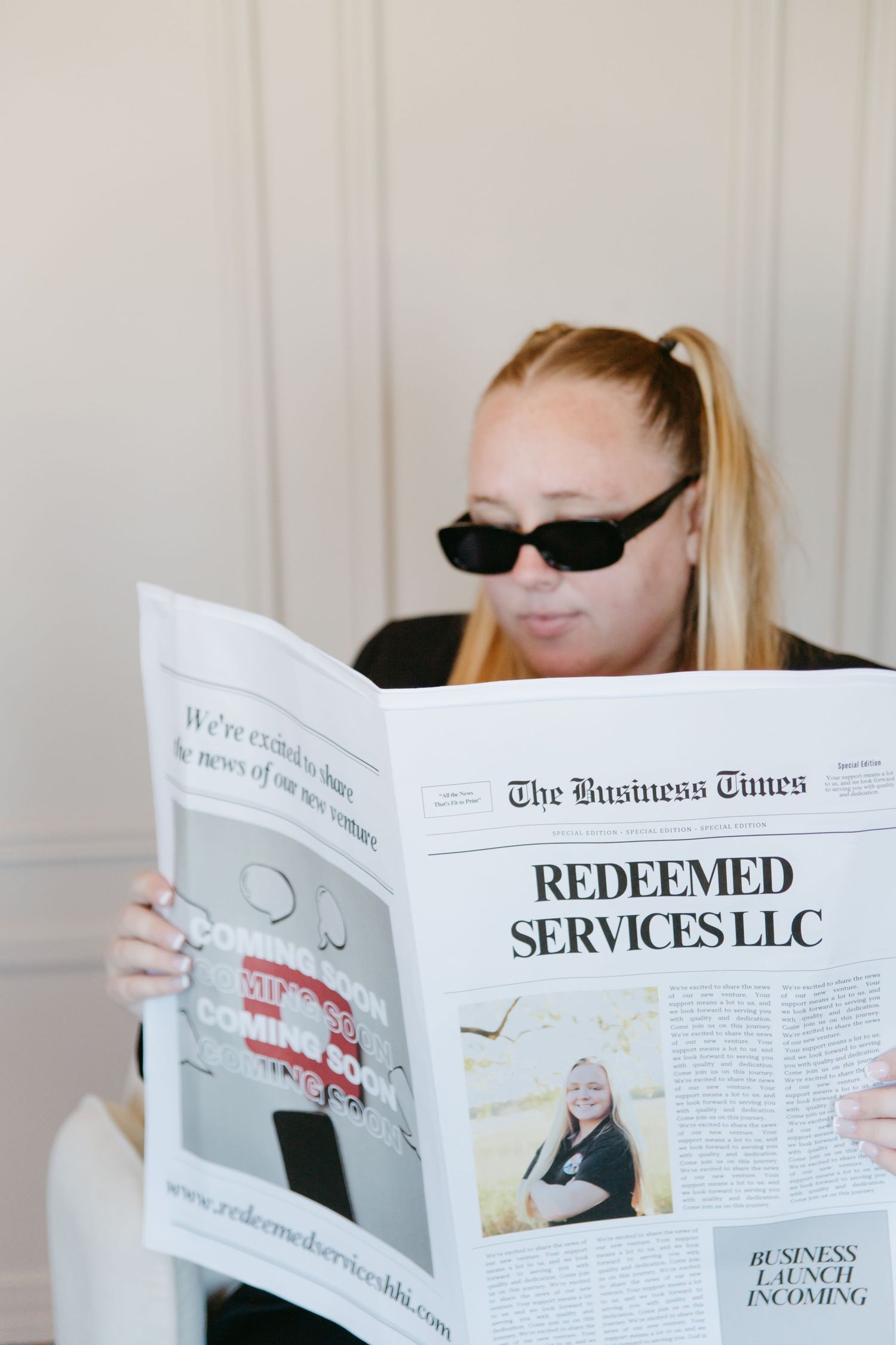 Woman in sunglasses reading The Business Times newspaper featuring Redeemed Services LLC business launch announcement.