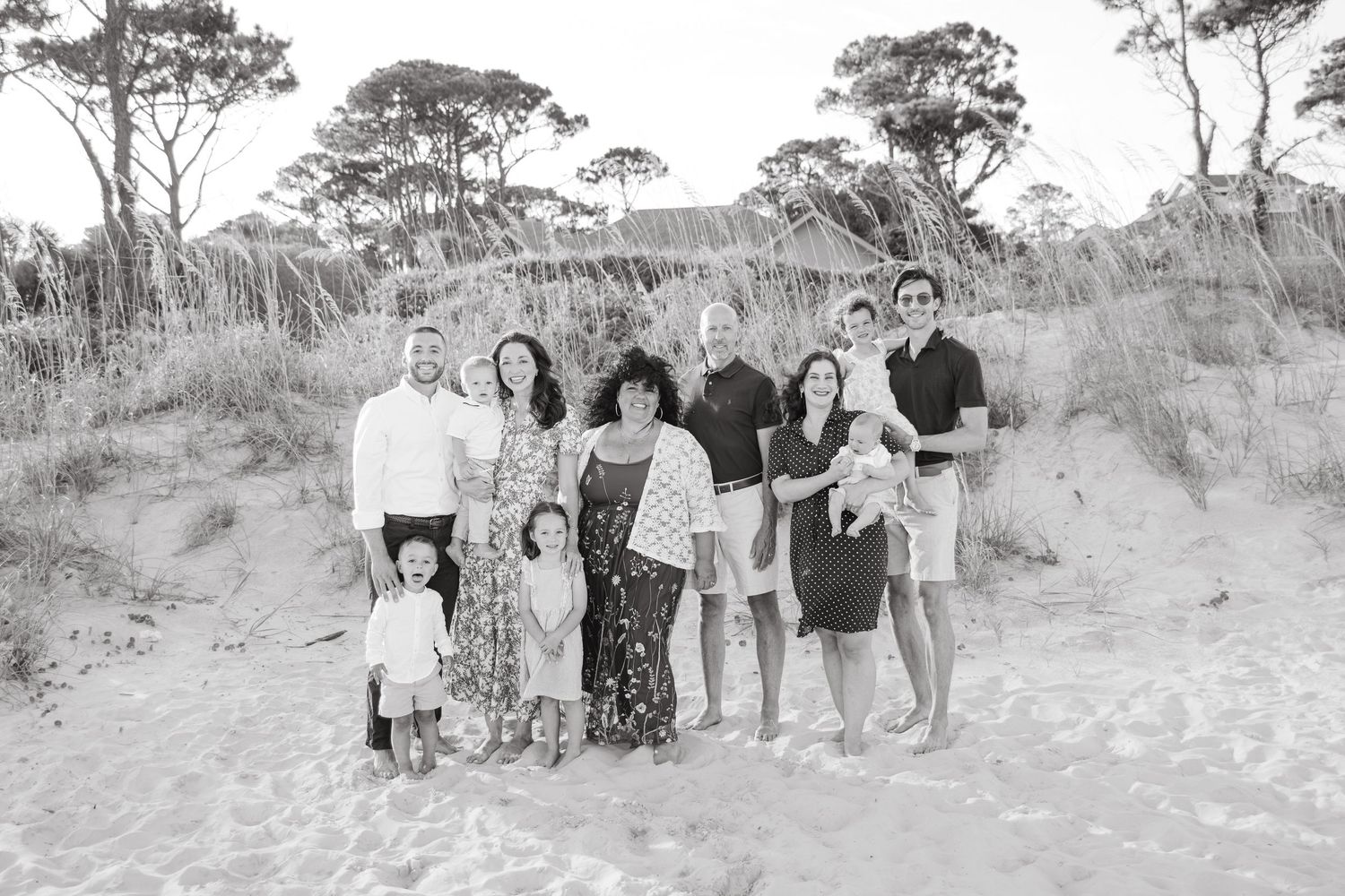 Black and white extended family portrait of adults and children gathered together on a sandy beach.