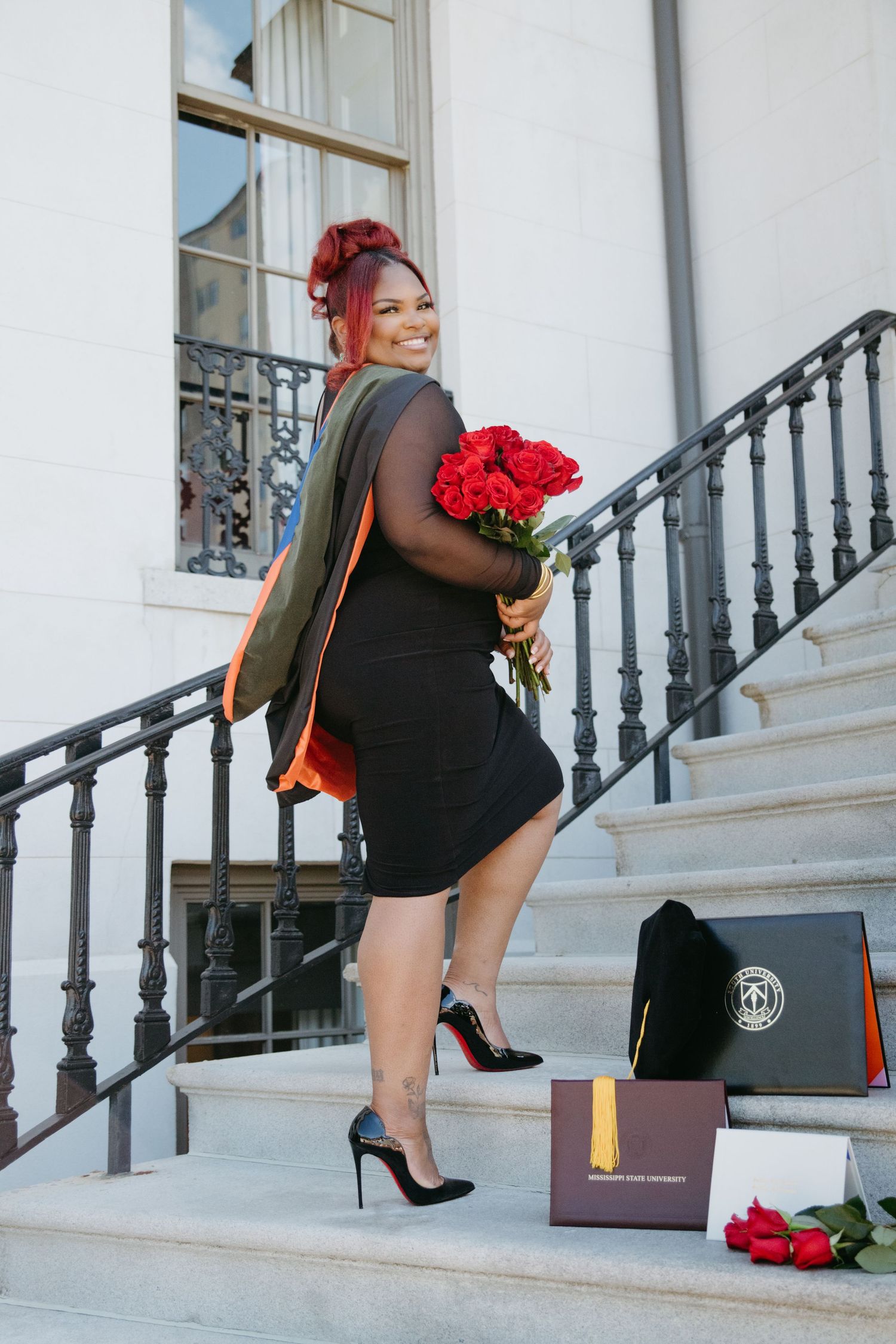Woman with red hair in black dress holding roses on steps with diploma box.