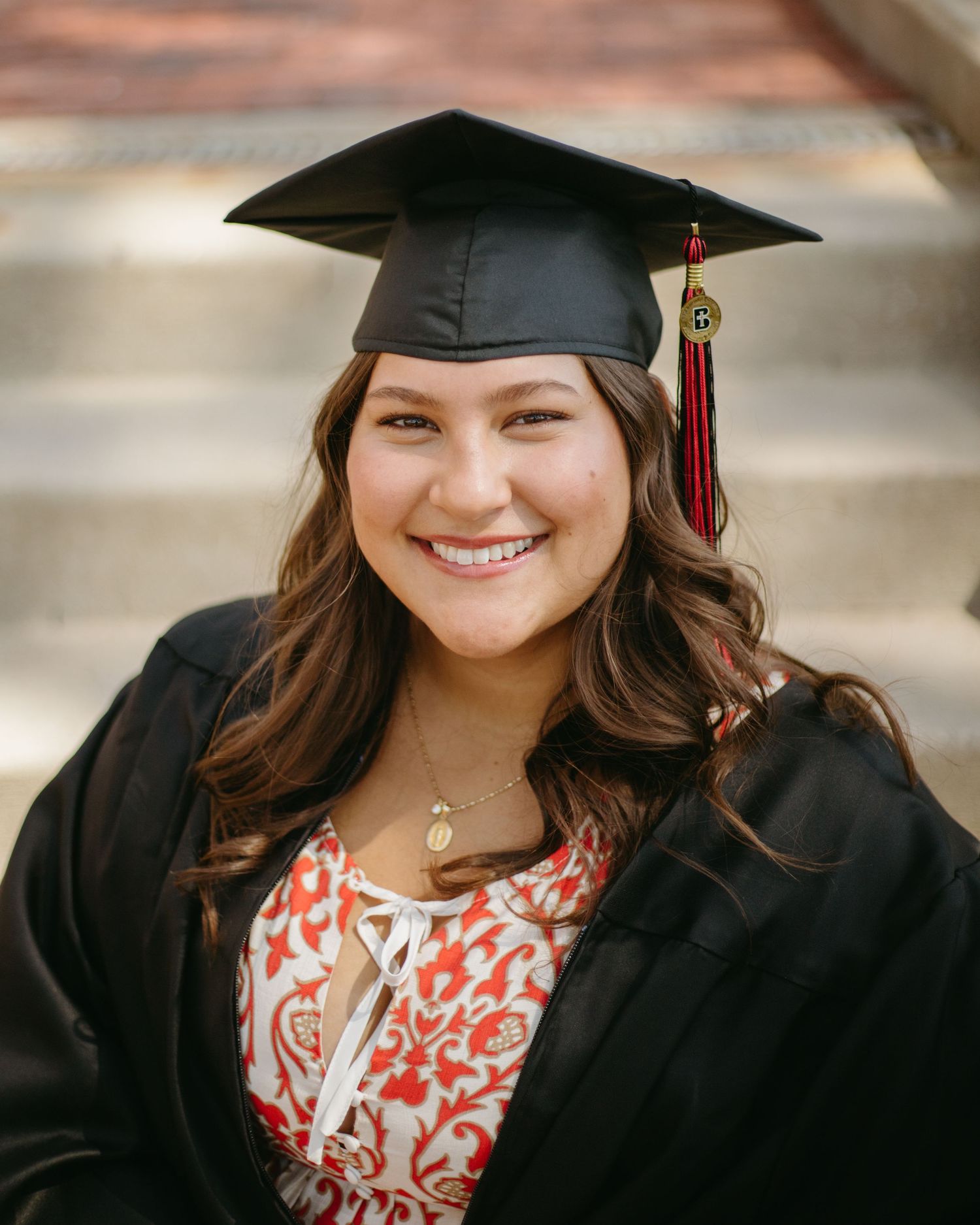 Smiling graduate in cap and gown with red tassel posing on steps for graduation portrait photo.