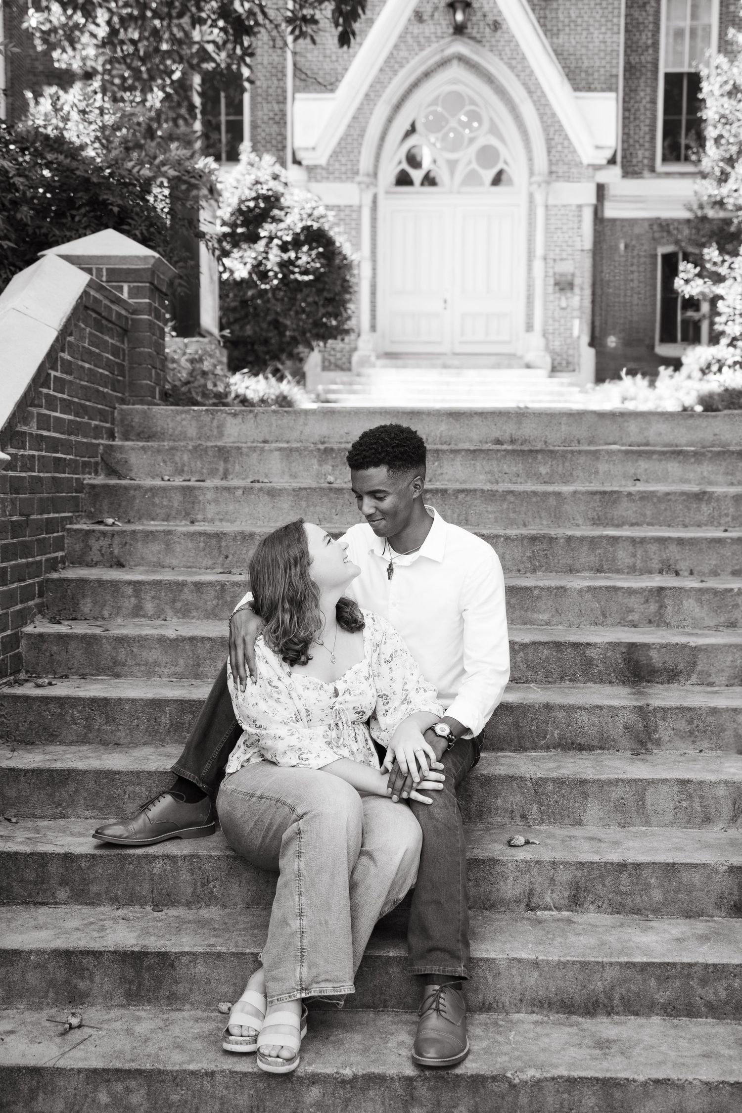 Black and white photo of couple kissing on stone steps in front of a Gothic church entrance.