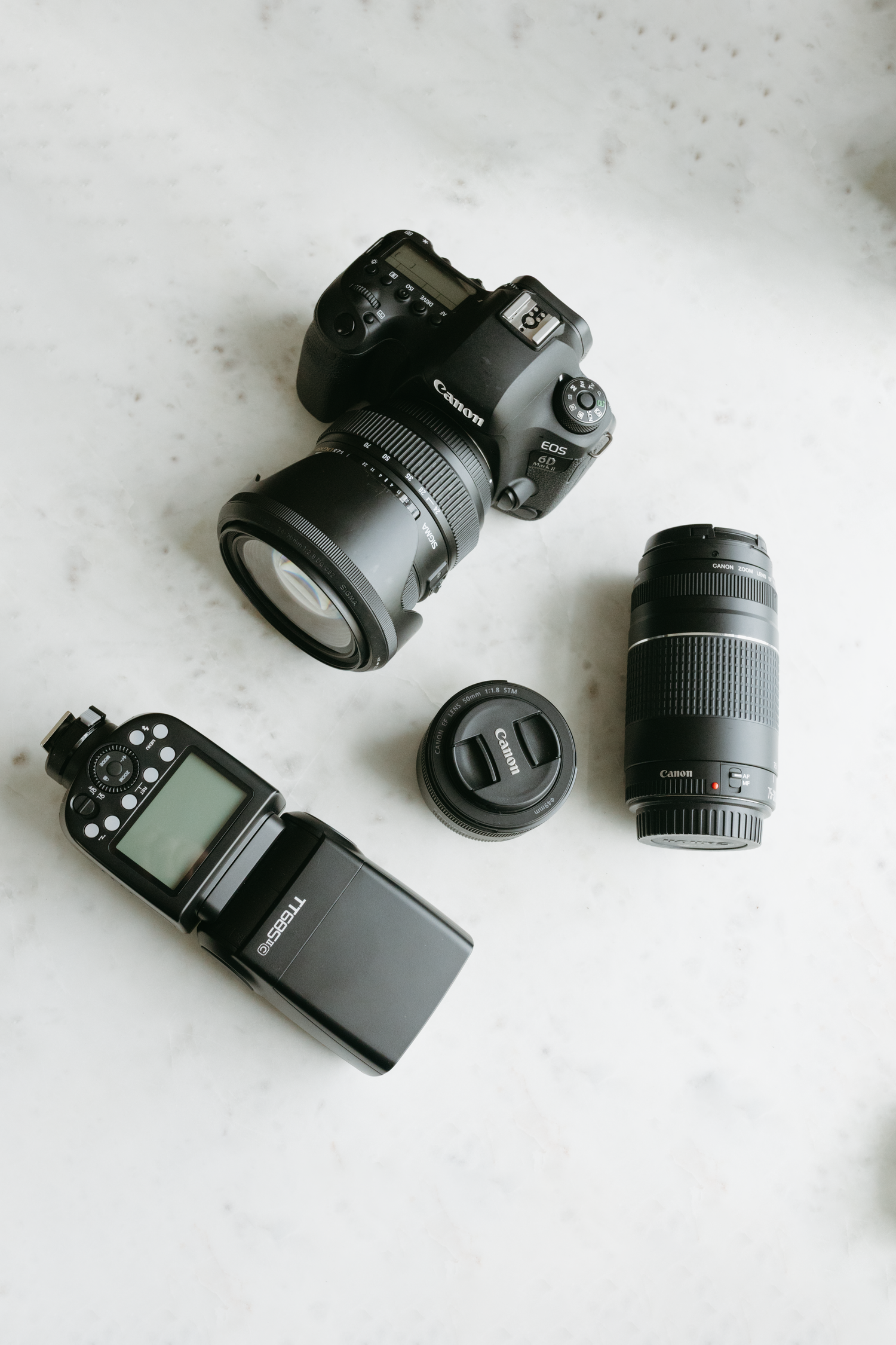 Canon DSLR camera with multiple lenses and external flash laid out on marble surface.
