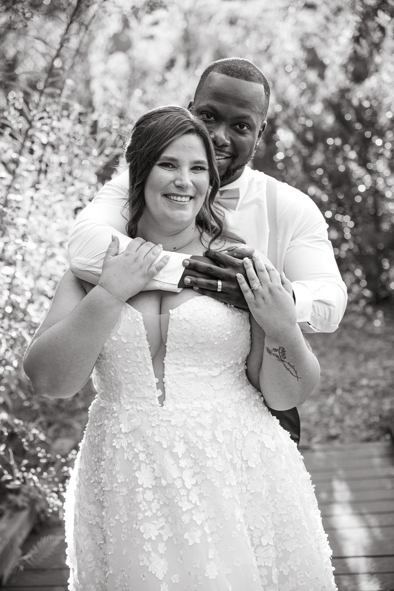 Black and white portrait of smiling bride and groom embracing outdoors showing wedding rings.