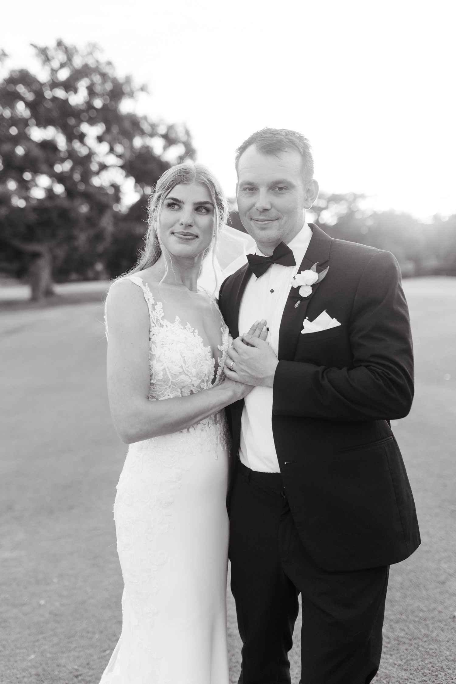 Black and white portrait of bride and groom posing elegantly outdoors at sunset after wedding ceremony.